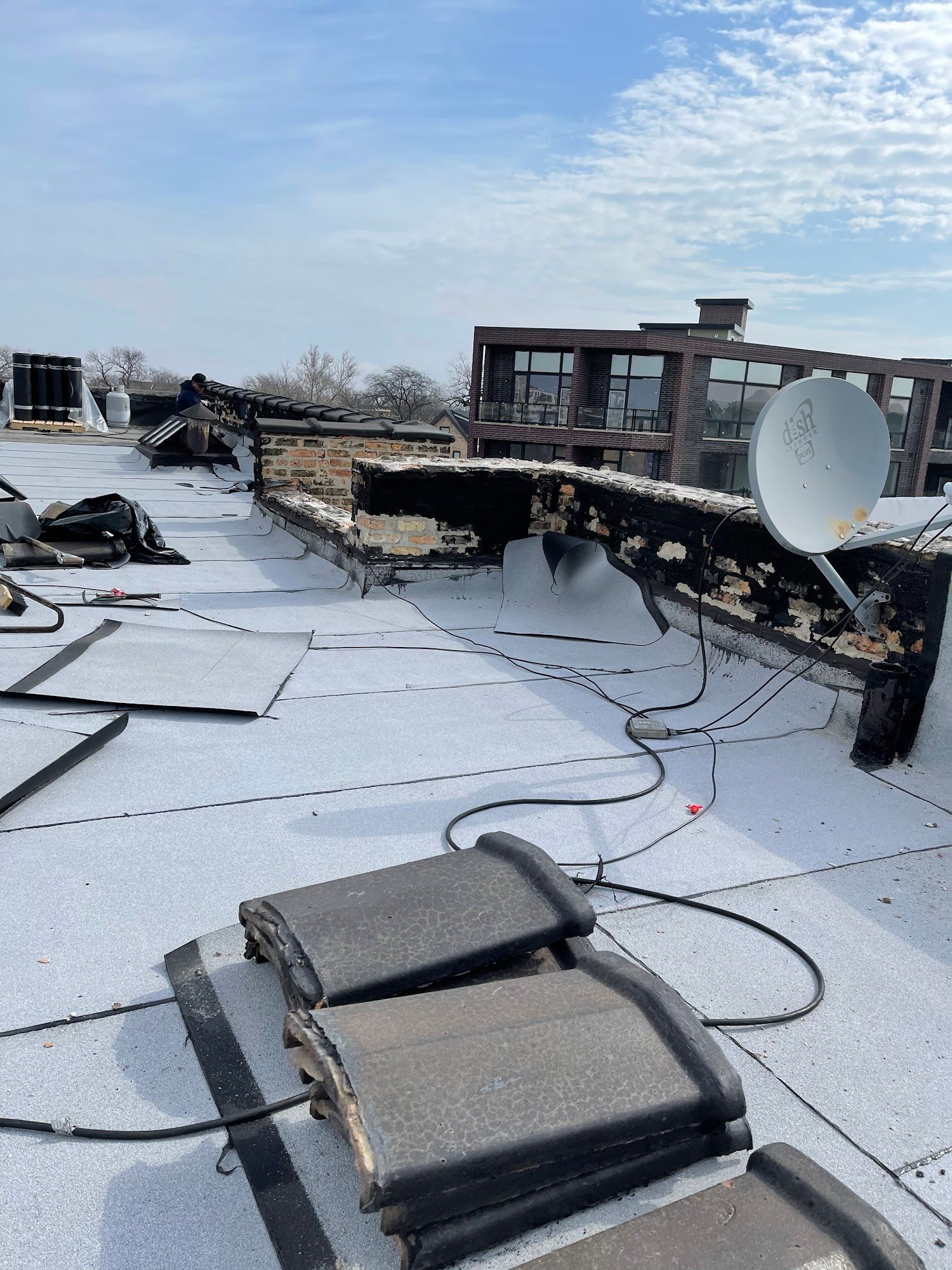 Snow-covered flat rooftop with HVAC units, cables, and a satellite dish under a cloudy sky