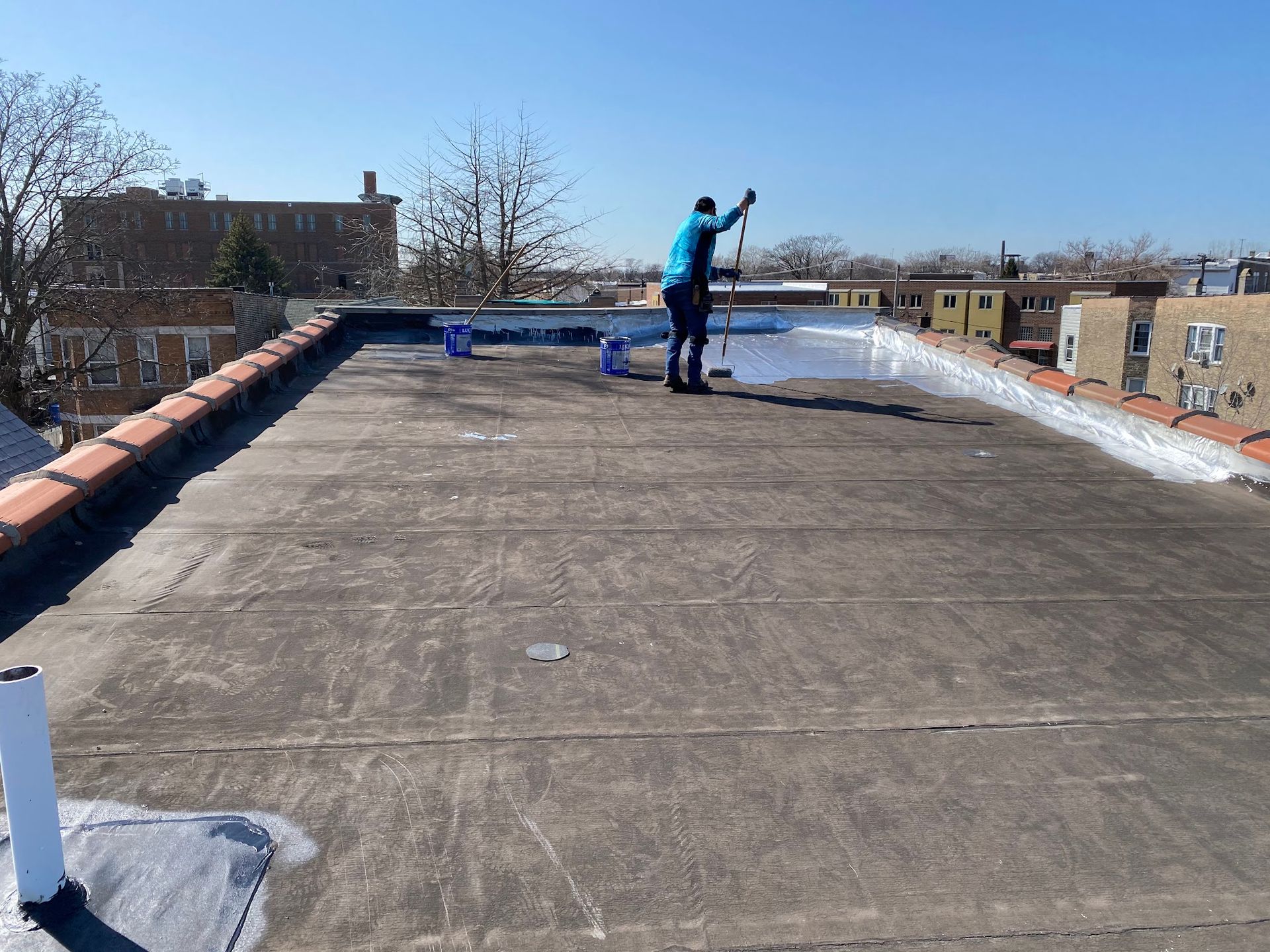 Worker applying coating on a flat rooftop under a clear sky