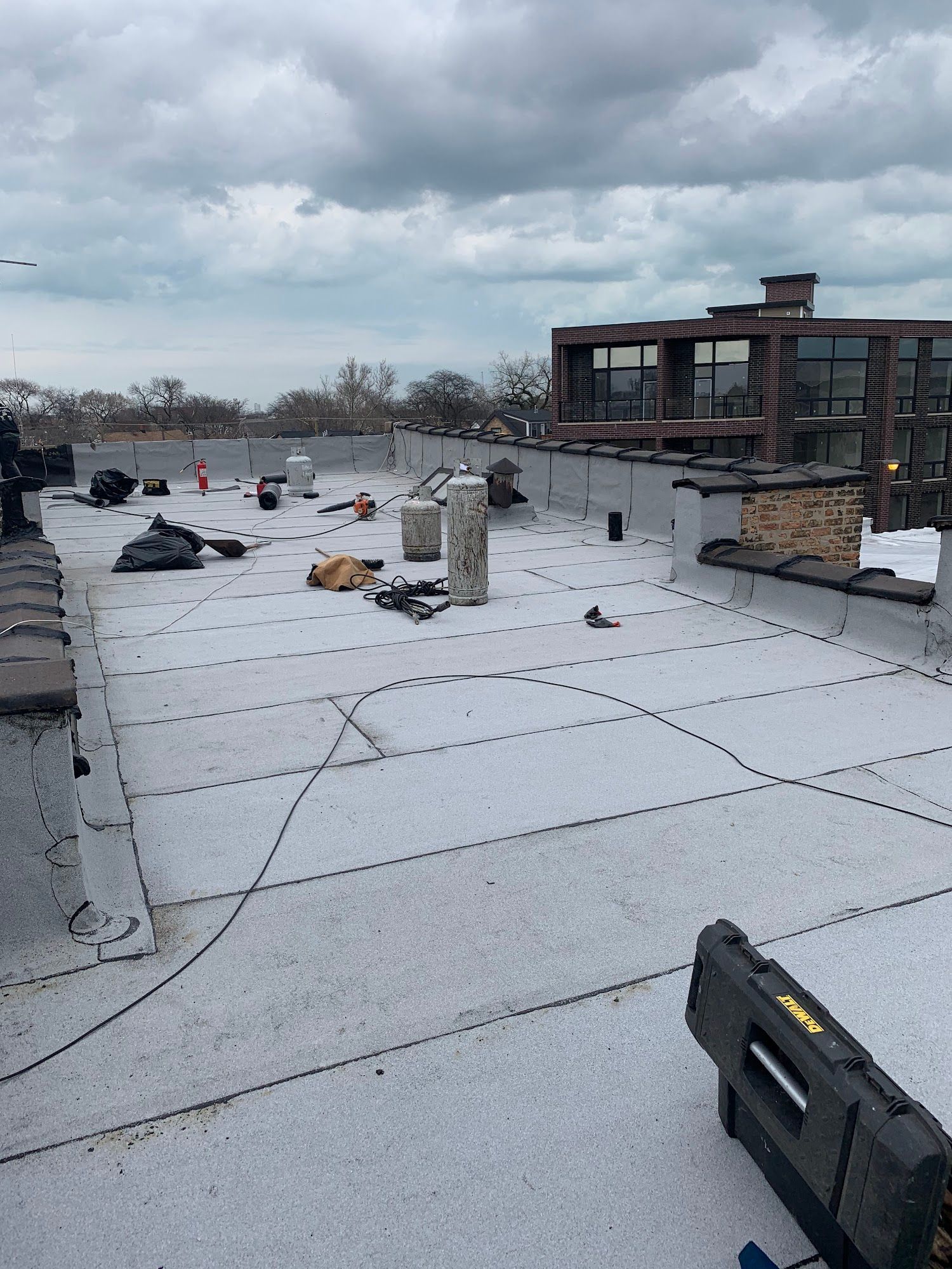 Flat rooftop under cloudy sky with roofing materials, tools, and a distant building facade