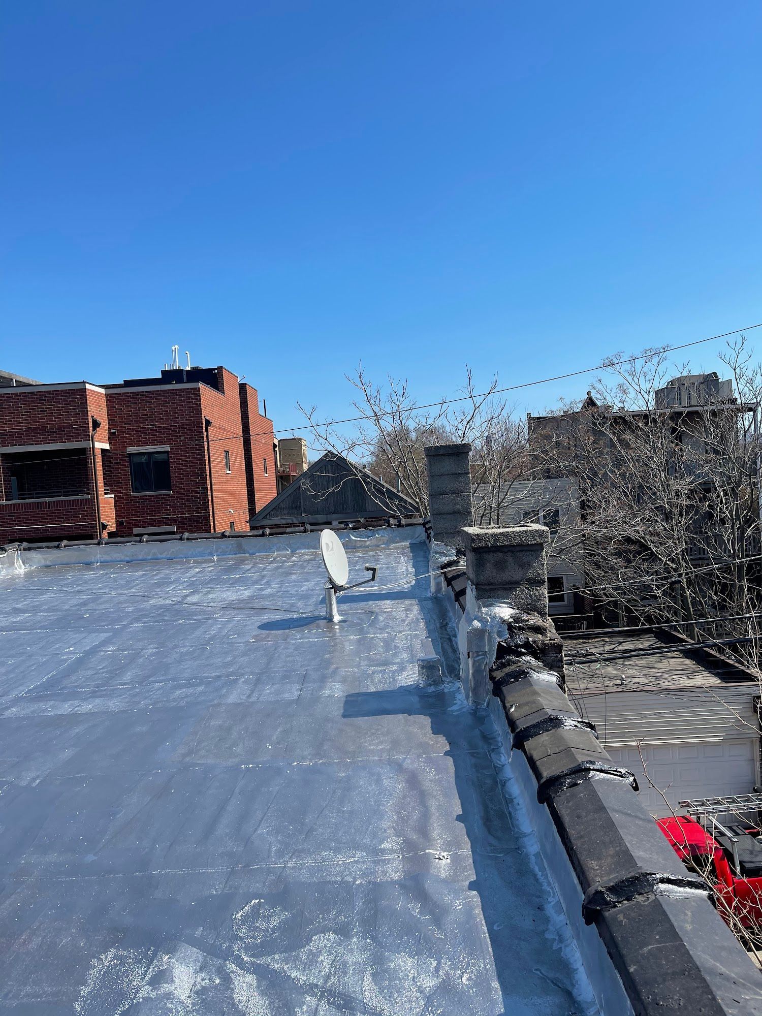 Flat rooftop with black membrane, brick buildings, and clear blue sky.