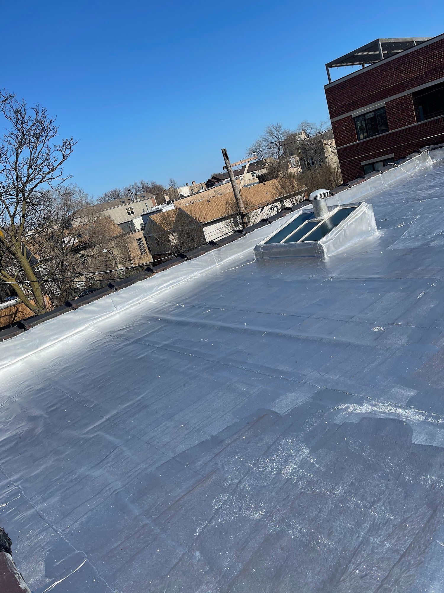 Flat rooftop with a skylight and surrounding brick buildings under a clear blue sky.