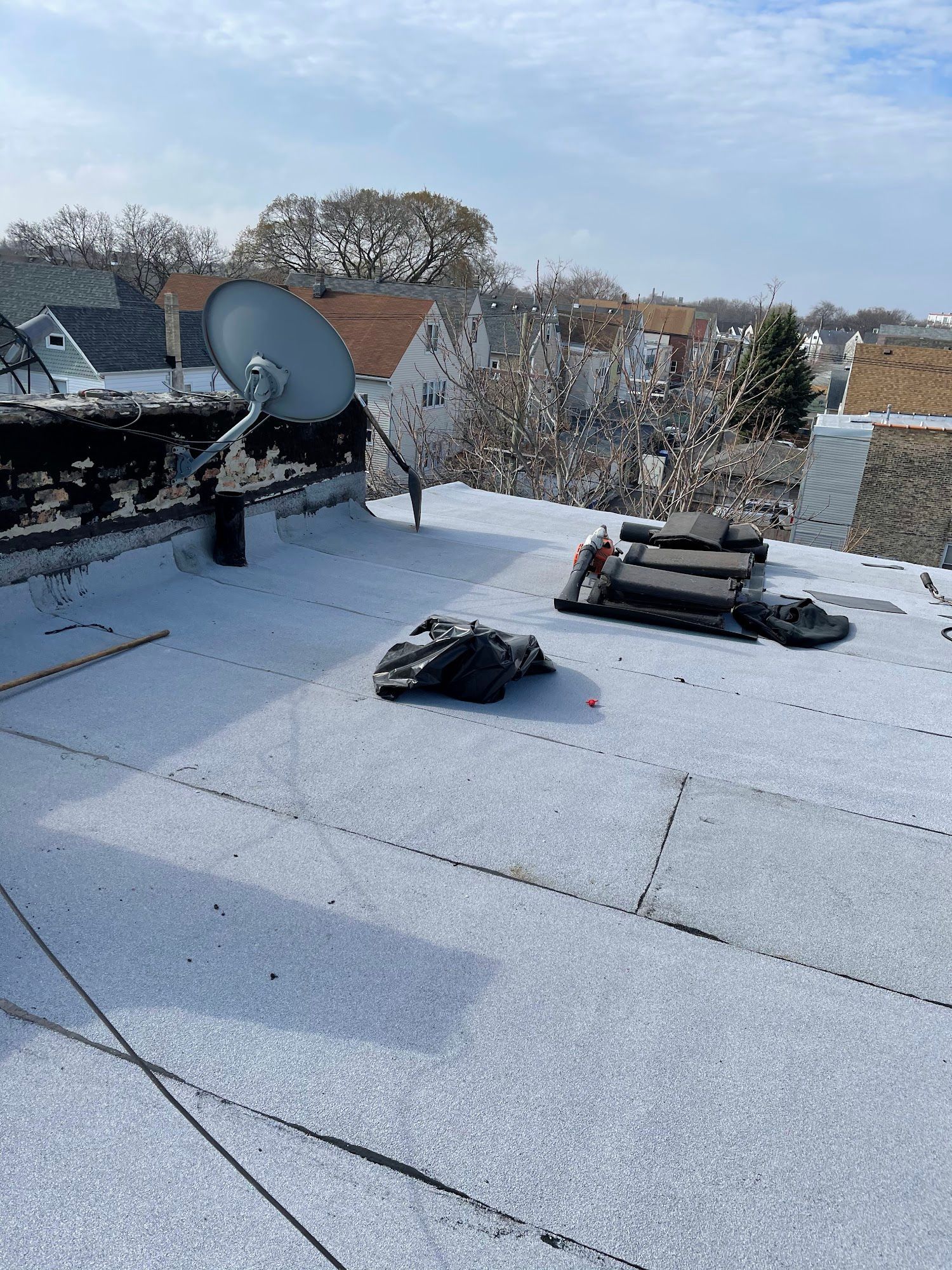 Snow-covered flat rooftop with satellite dish, vents, and city buildings in the distance