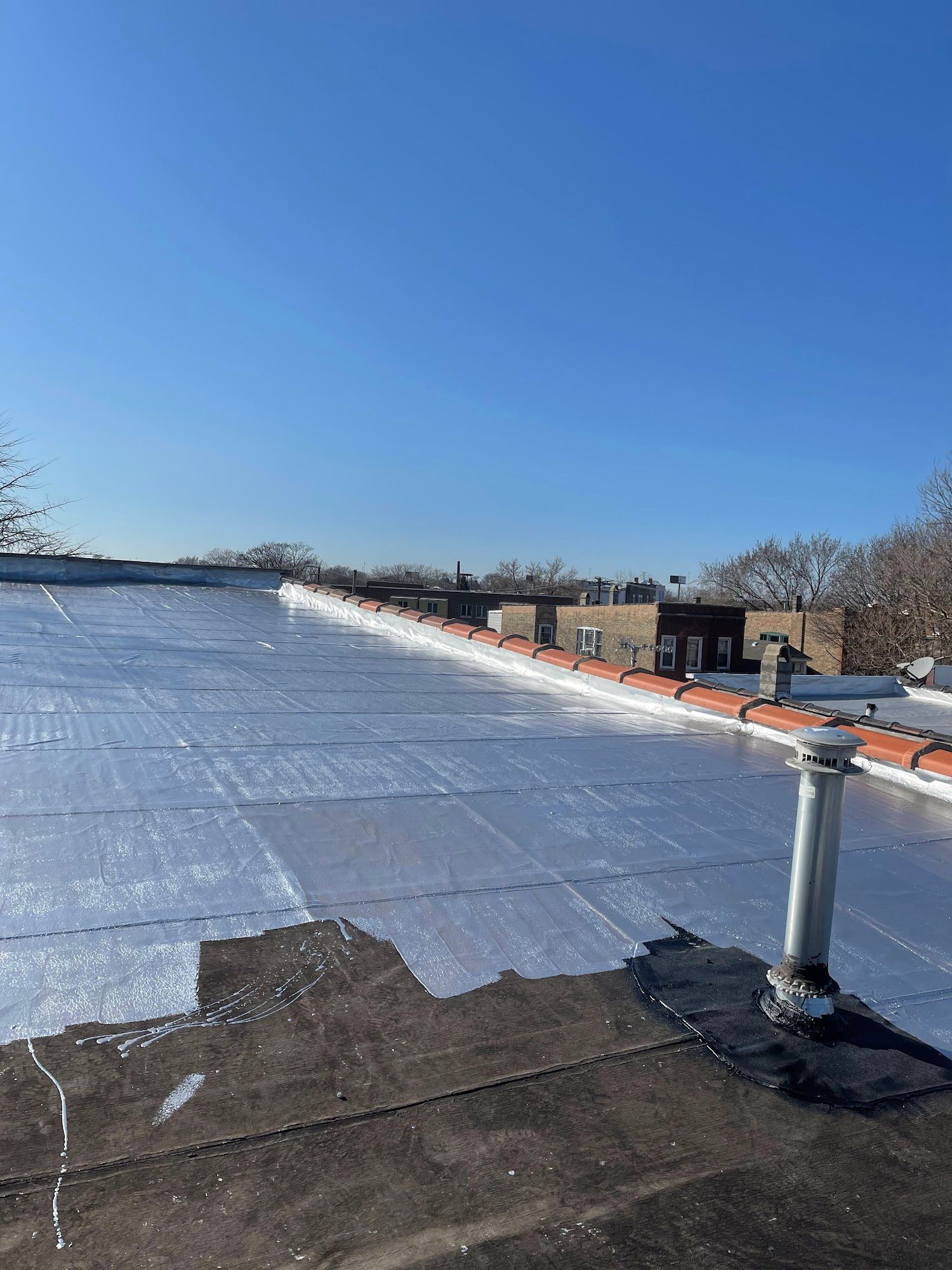 Rooftop covered with silver reflective insulation under a clear blue sky, with vents and low buildings nearby.