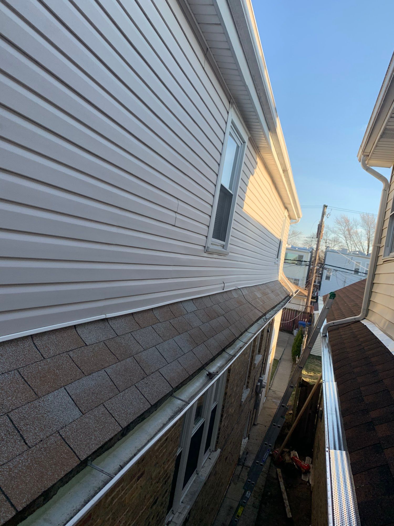 Narrow side view between two houses with vinyl siding and a shingled roof, showing a small yard below