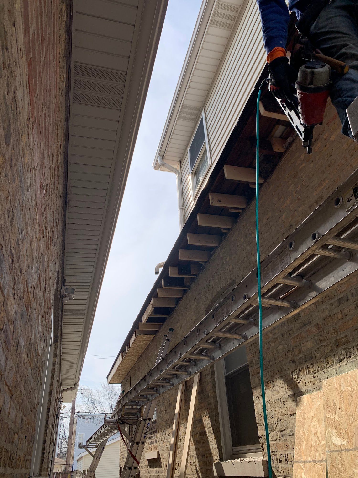 Worker on a roof between narrow stone buildings, using a rope and harness.