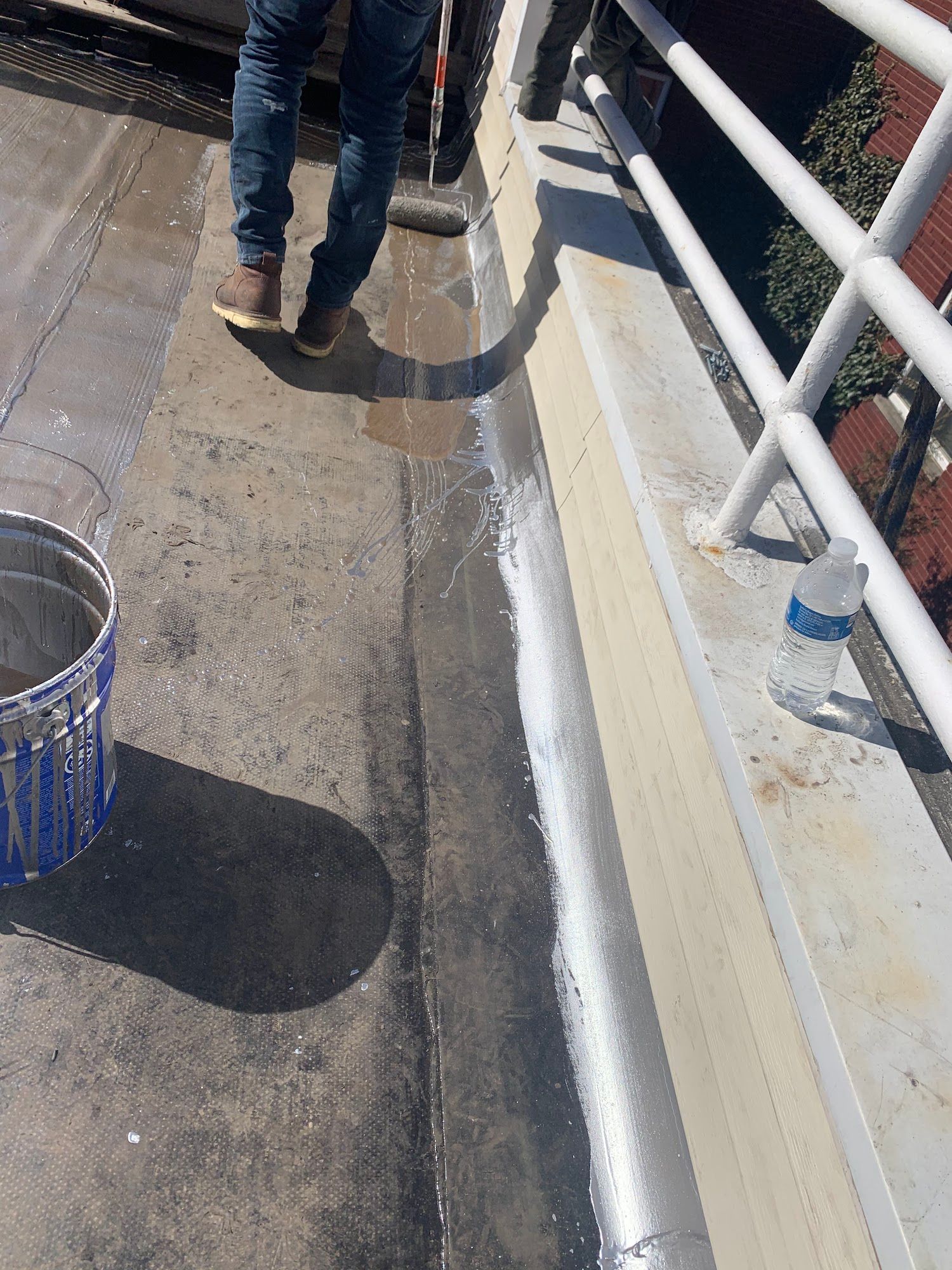 Person walking on a sunny sidewalk beside a railing and trash can.