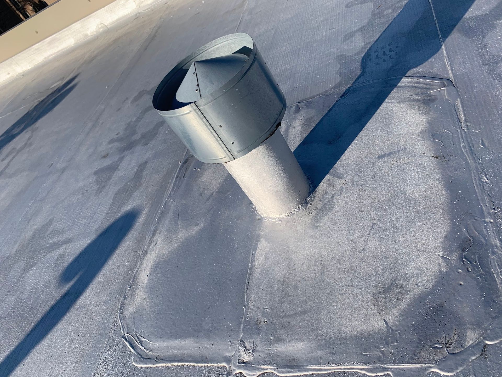 Rooftop vent pipe with a metal cap on a flat white roof, casting a long shadow.