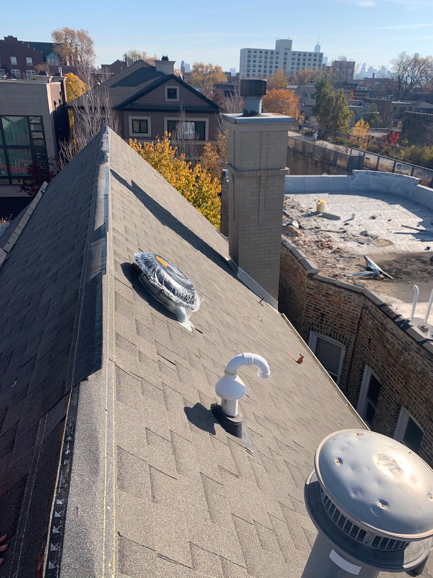 Rooftop view with gray shingles, vents, and a chimney overlooking houses and snowy ground under a clear sky