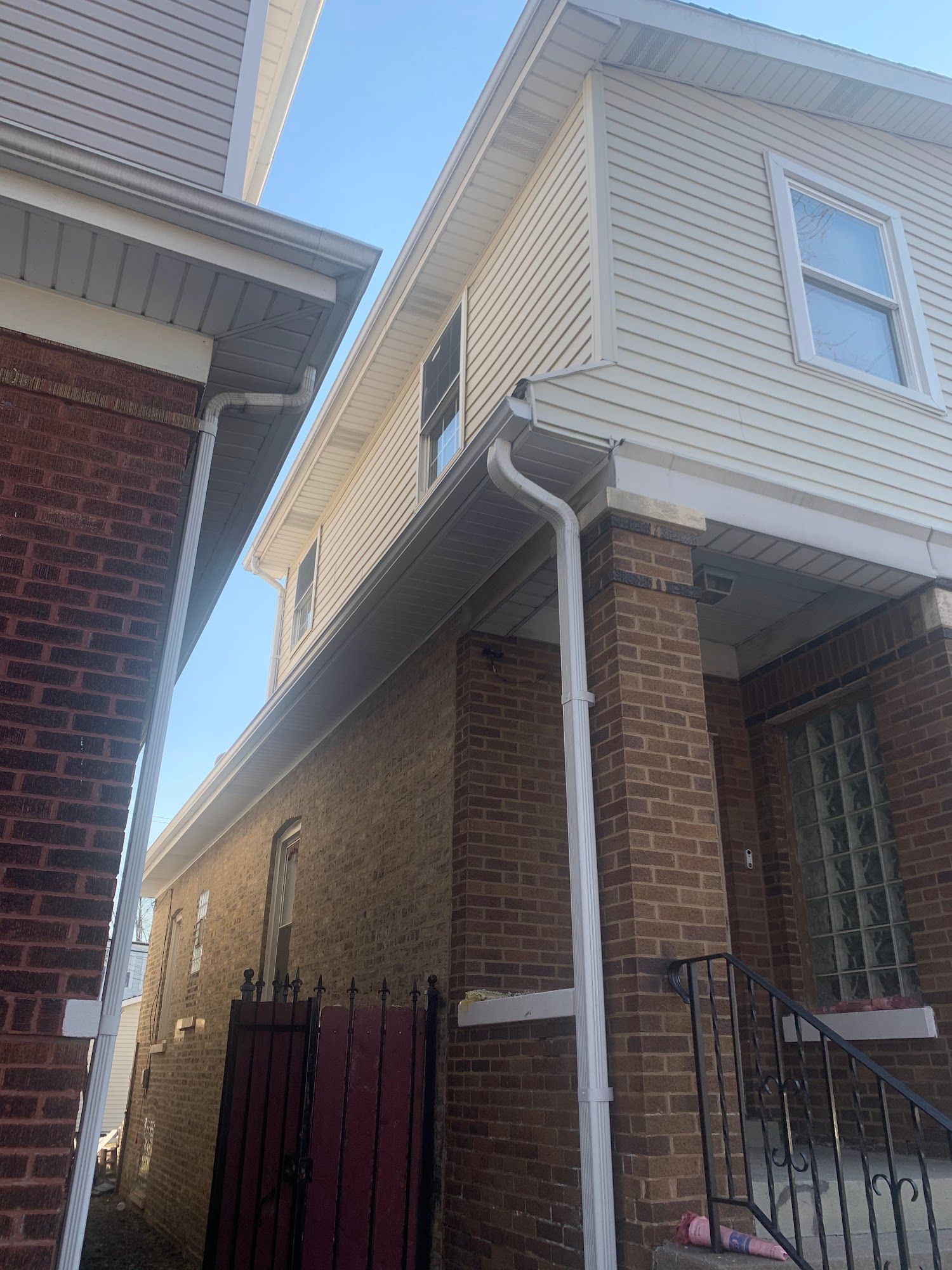 Two brick houses with white siding and roof eaves, viewed in a narrow side alley.