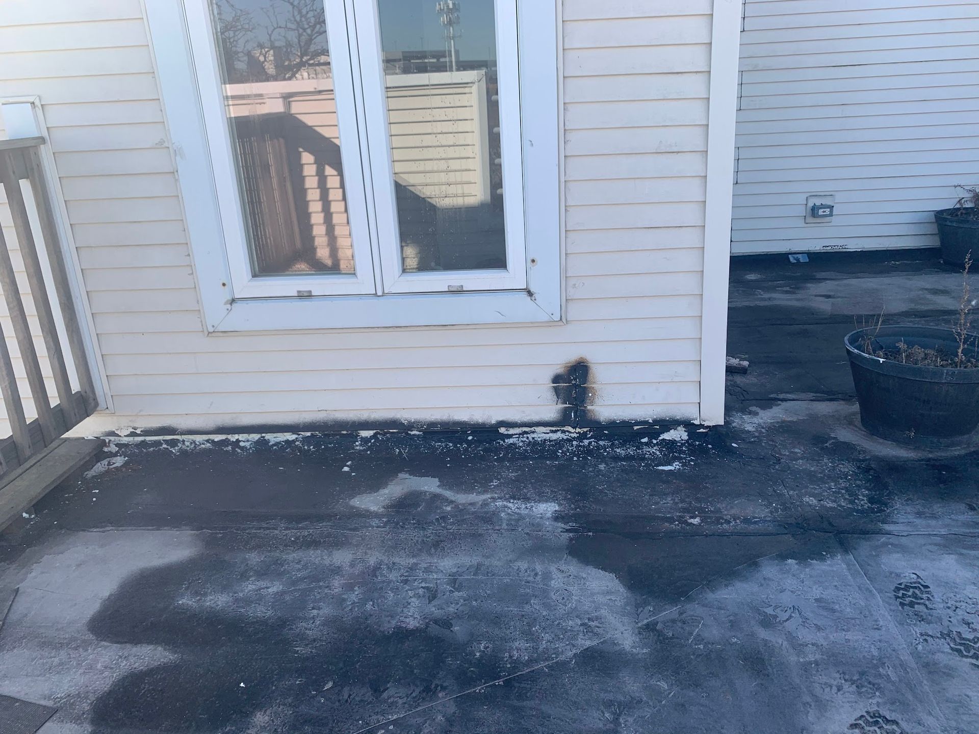Snow-dusted patio outside a house with white siding and a double glass door.