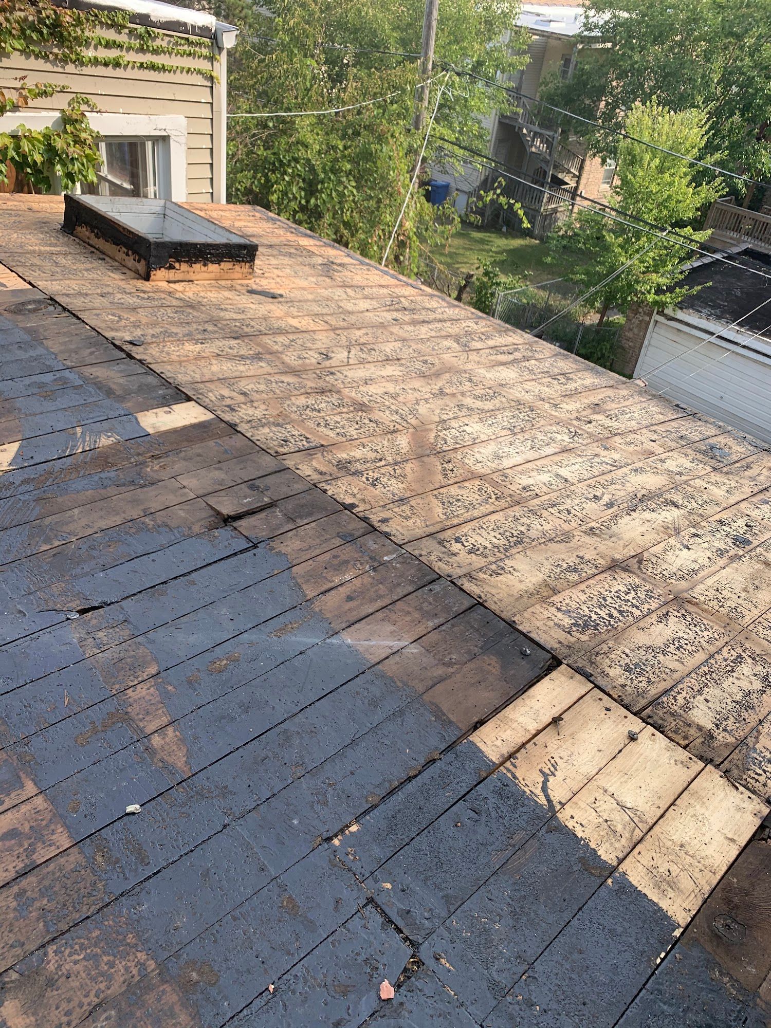 Damaged rooftop with exposed underlayment and loose shingles beside a small rooftop vent.