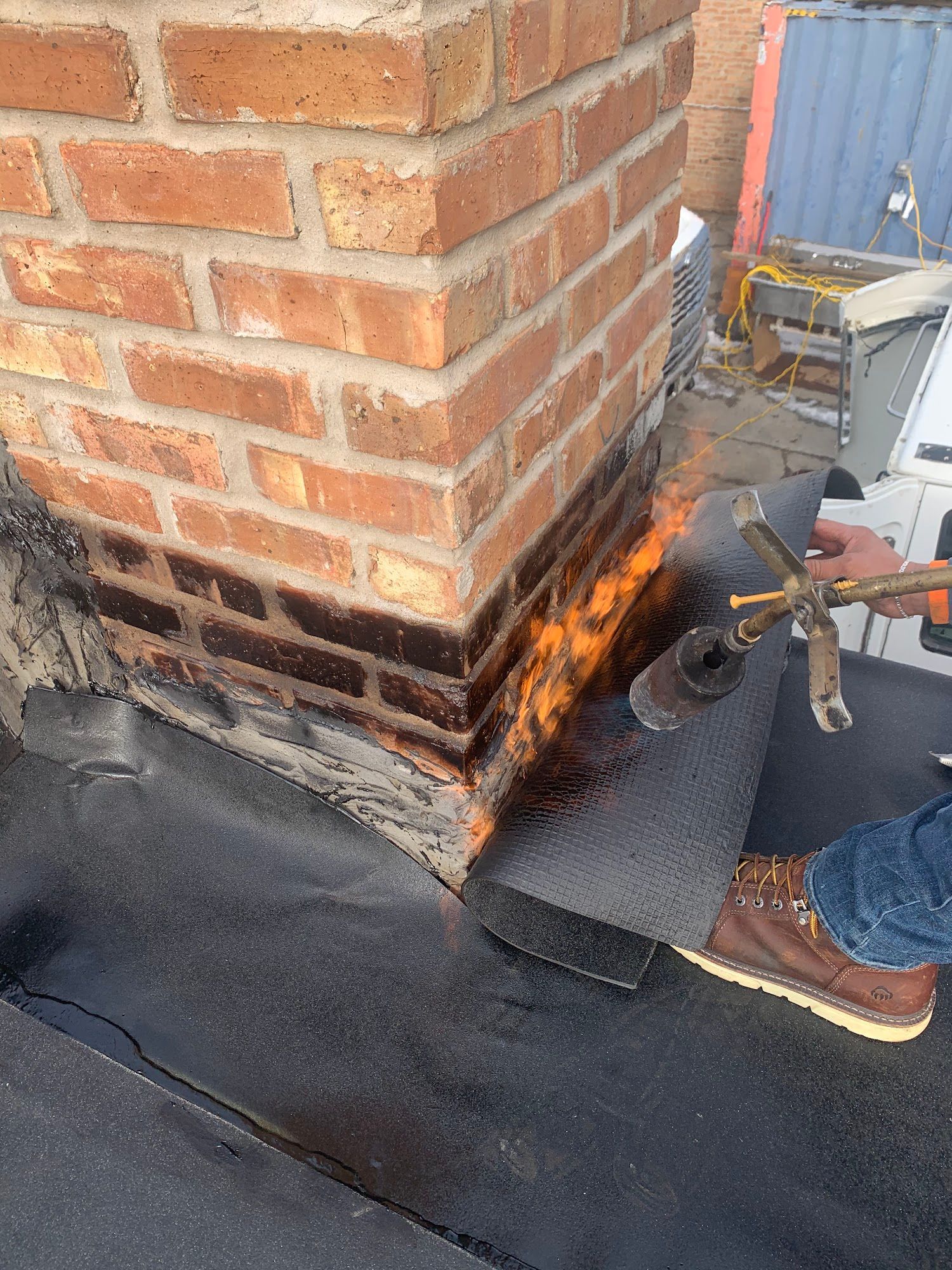 Worker using a torch to repair flashing around a brick chimney on a roof