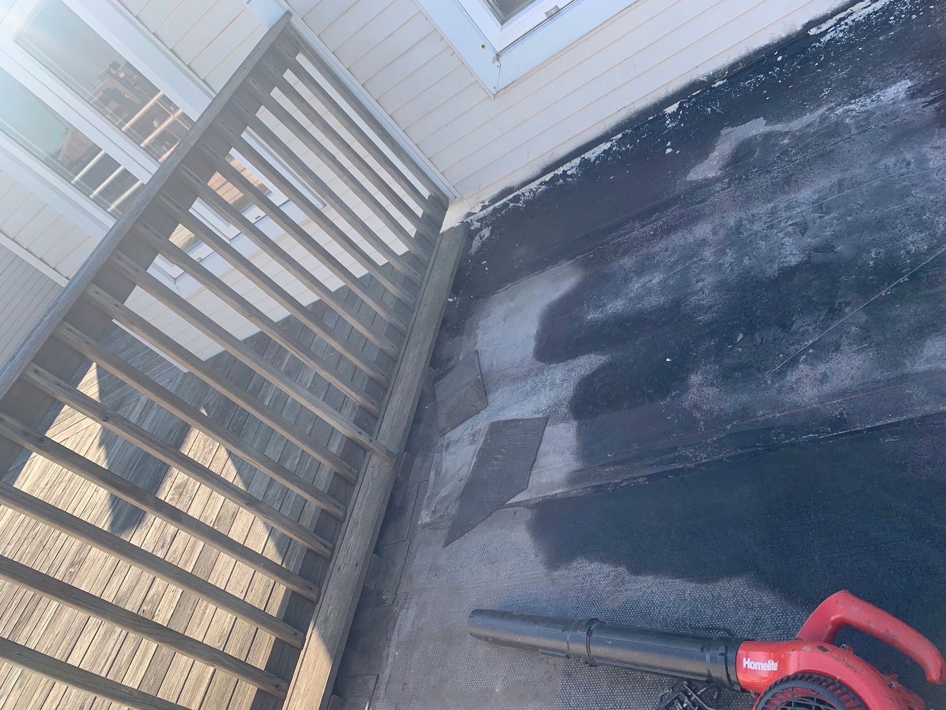 Exterior stairwell with metal railing and a red shovel on a black asphalt roof surface.