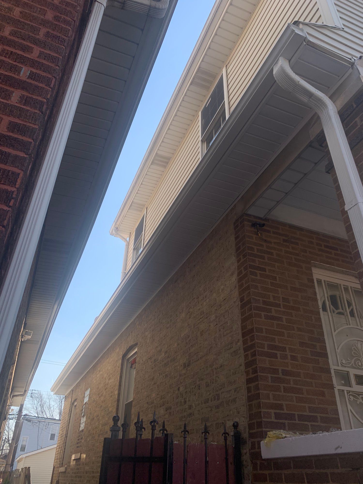 Narrow alley between brick houses with a black metal fence and blue sky overhead