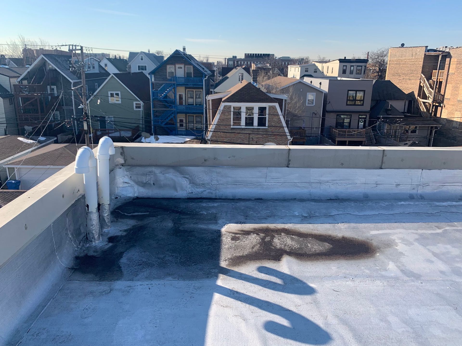 Rooftop with snowy parapet and a view of houses under a clear blue sky