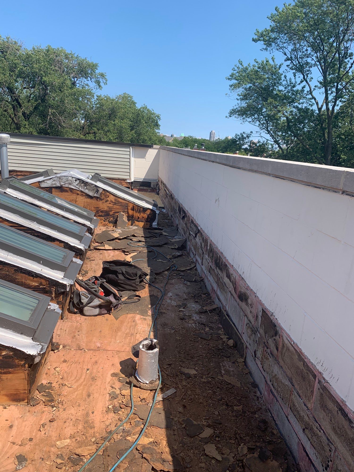Rooftop under repair with exposed materials, skylights, and a long white parapet wall.