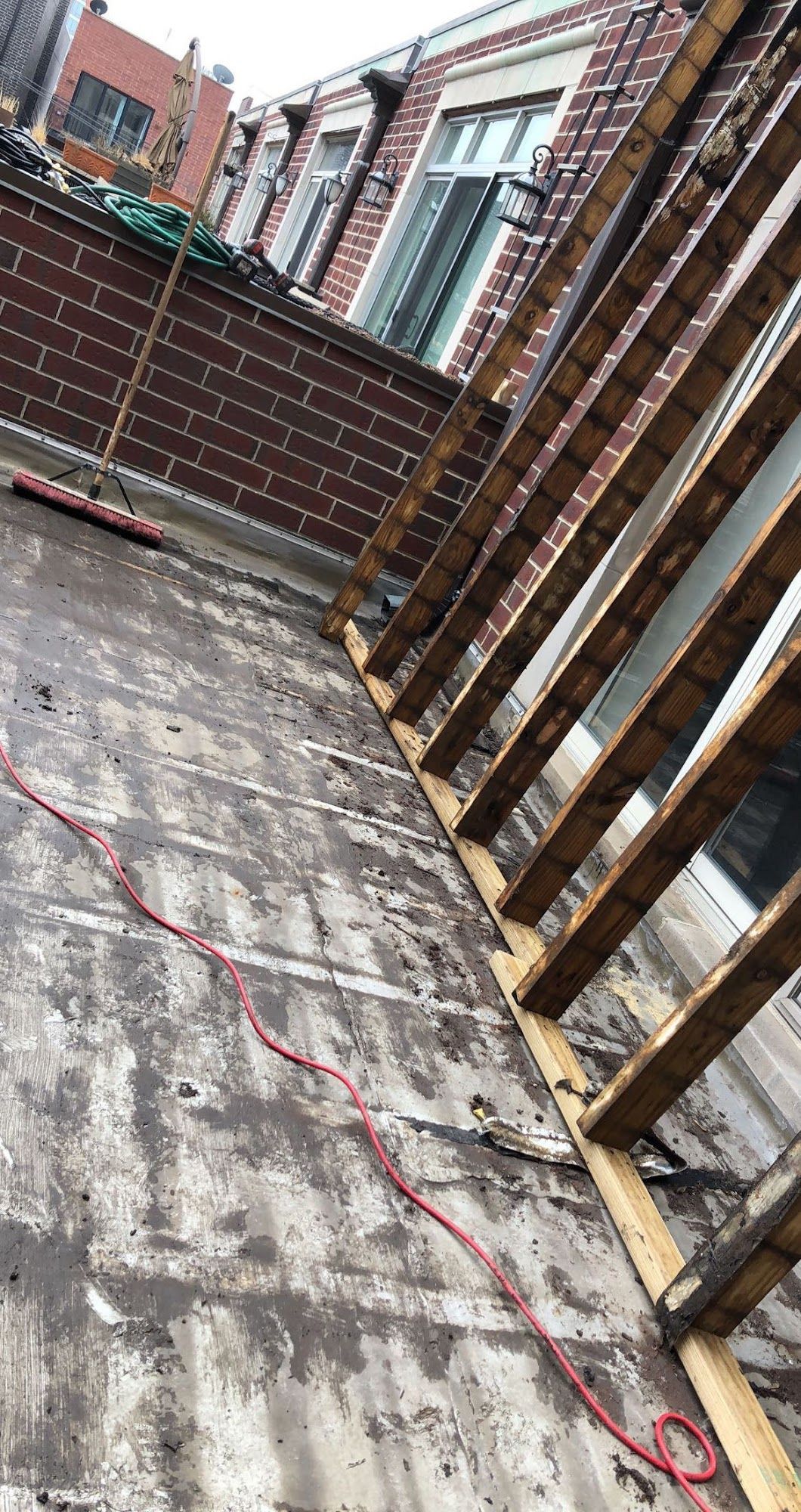 Rooftop deck with weathered concrete floor and wooden railing beside brick buildings.