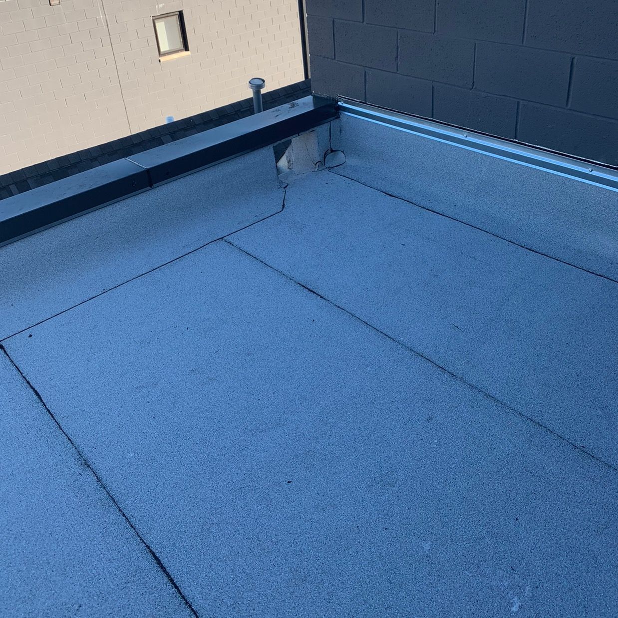 Blue flat roof with gravel surface, parapet walls, and a vent near the corner.