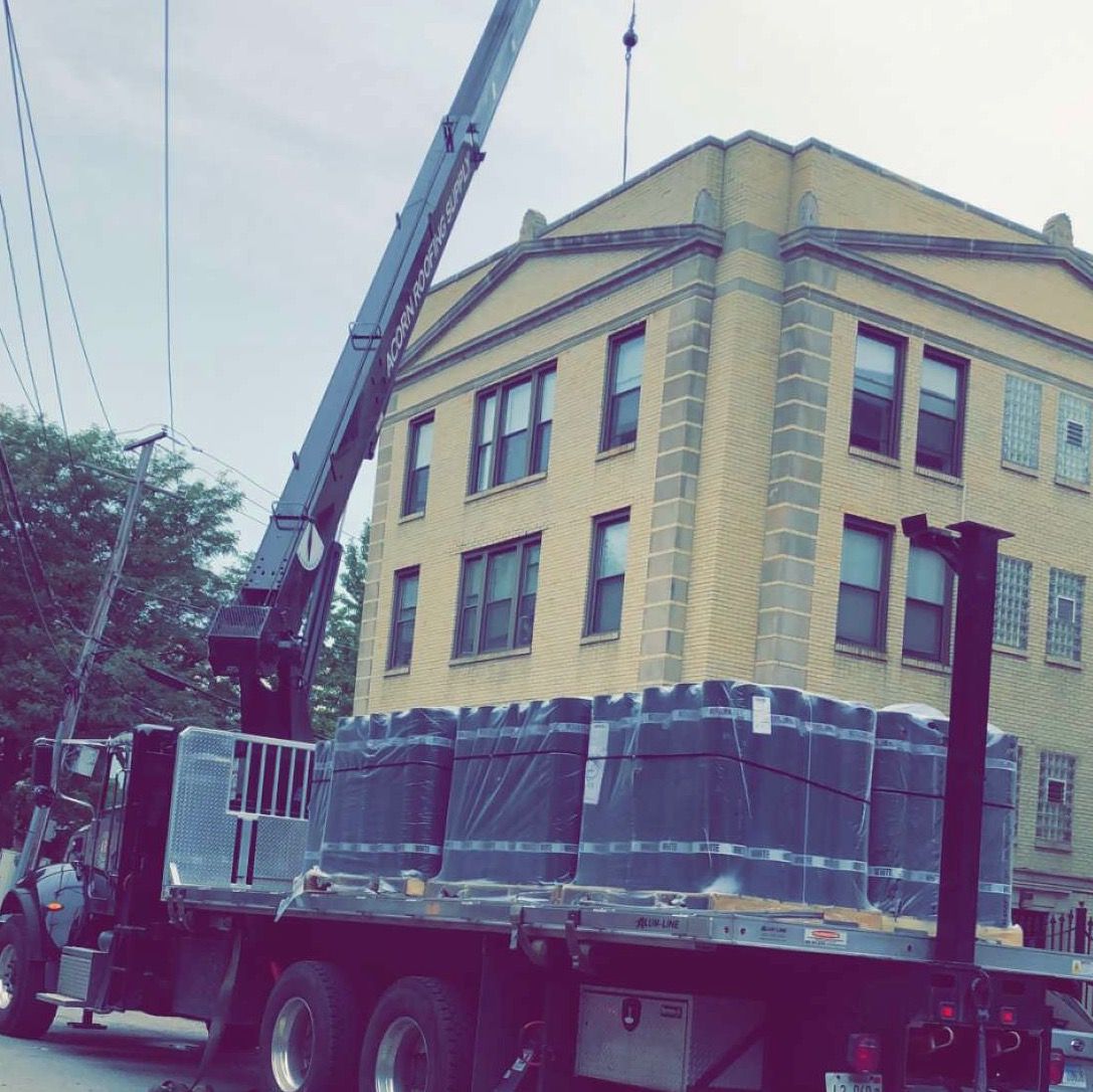 Yellow building on a flatbed truck, wrapped in protective sheeting and lifted by a crane on a street.