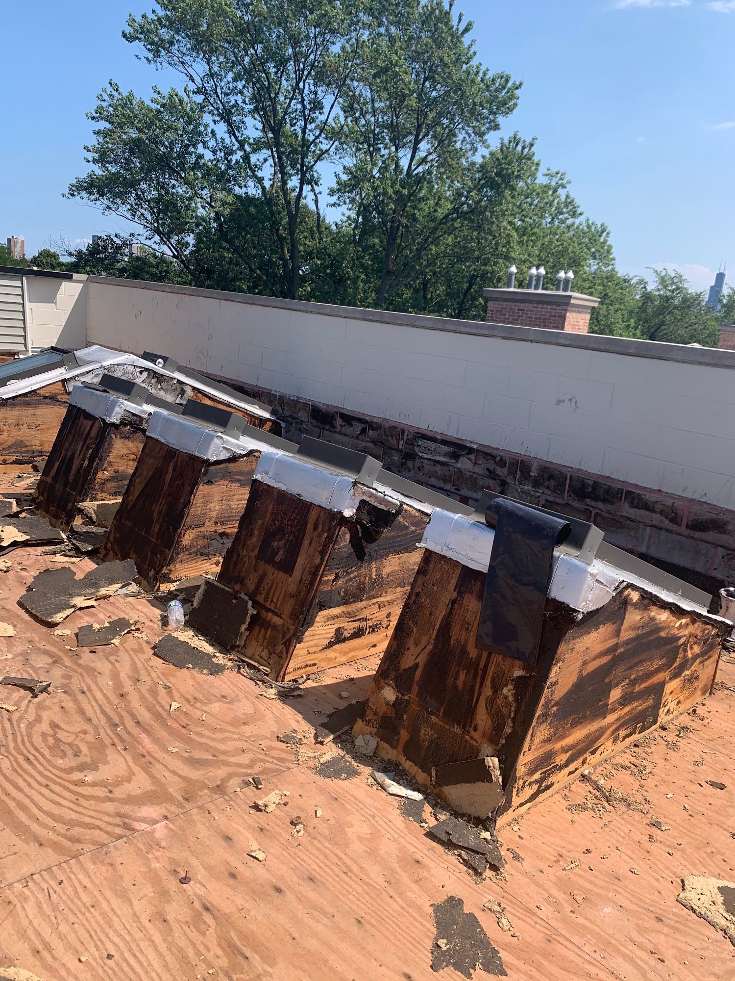 Roofing work in progress on a low building, with exposed wooden framing and tar paper under a blue sky