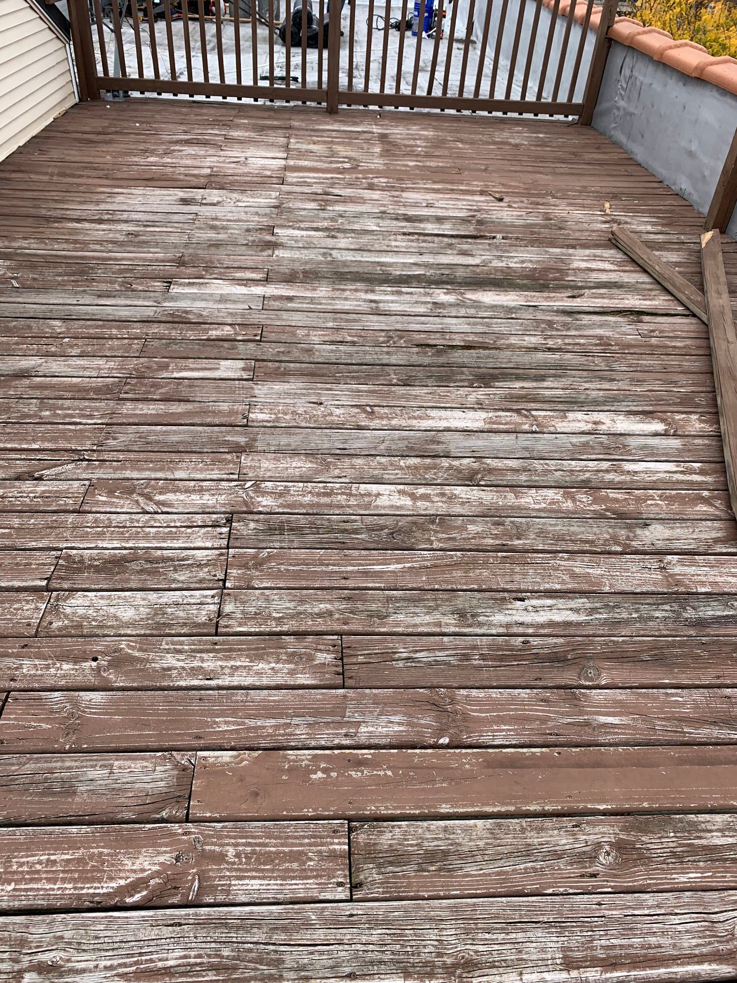 Weathered wooden deck with peeling paint and a railing overlooking snow outside.