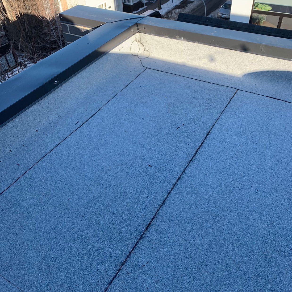 Blue-tinted rooftop with gravel surface and black metal railing in sunlight