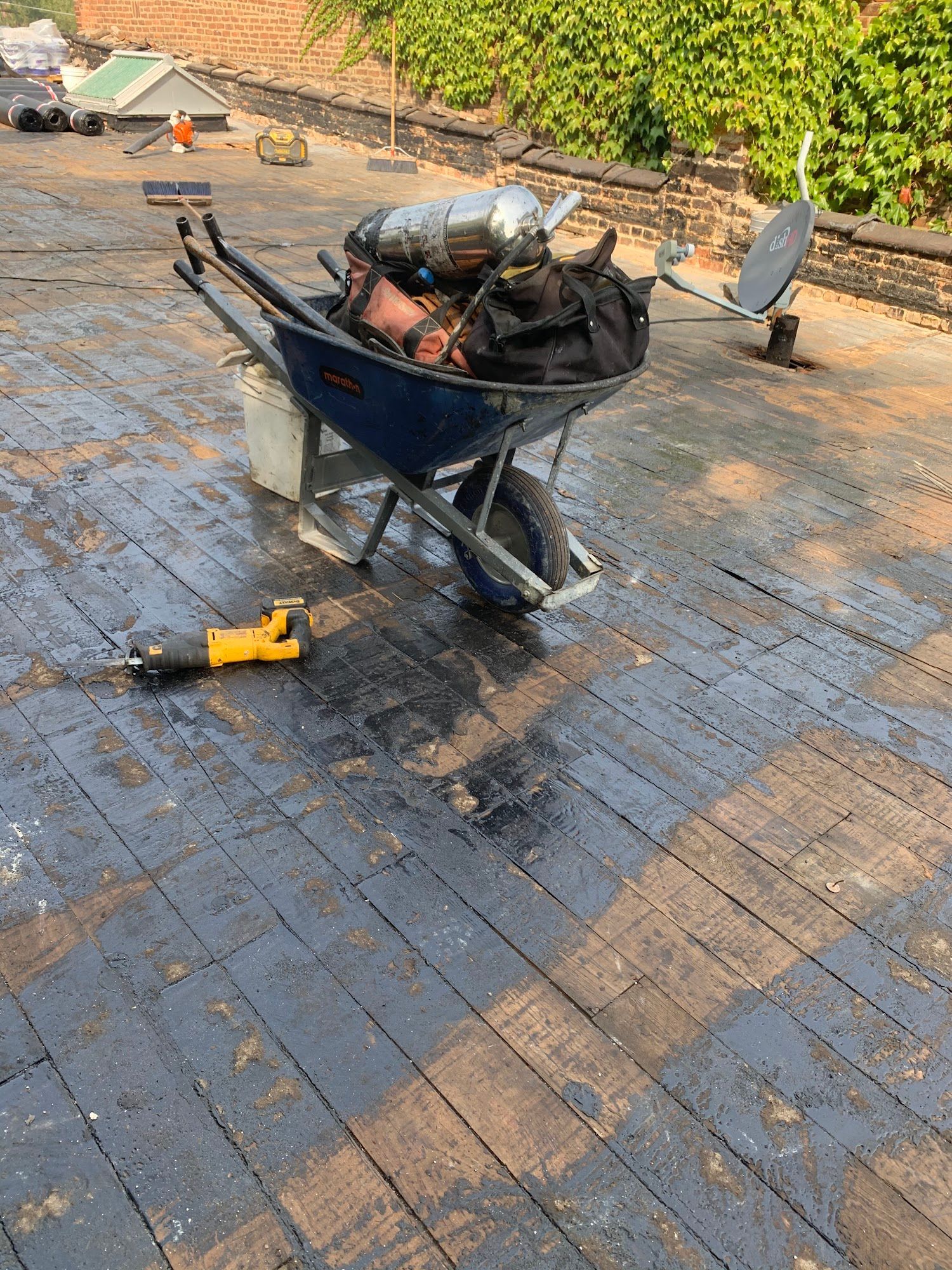 Wheelbarrow of burned debris on a tiled rooftop, with a yellow power tool nearby and a satellite dish in back