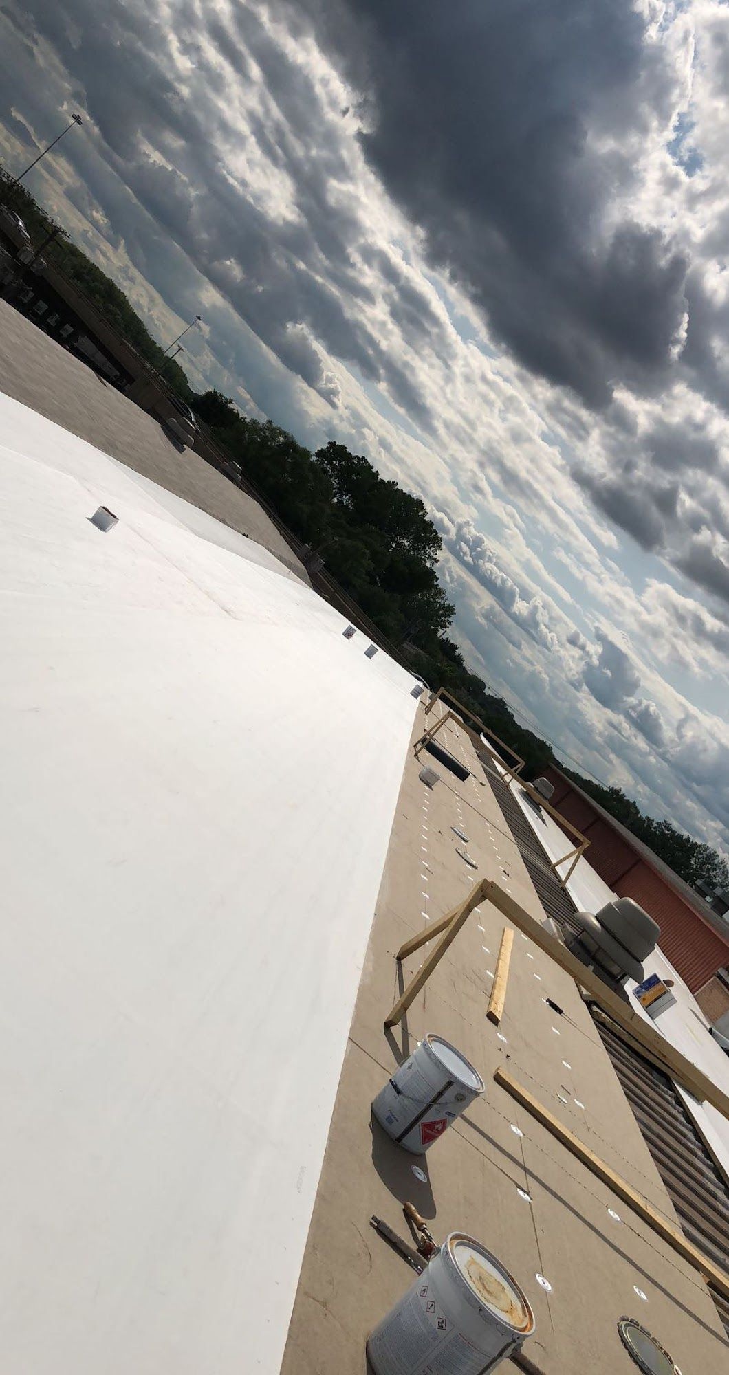 Tilted rooftop with white membrane, vents, and cloudy sky over nearby buildings.
