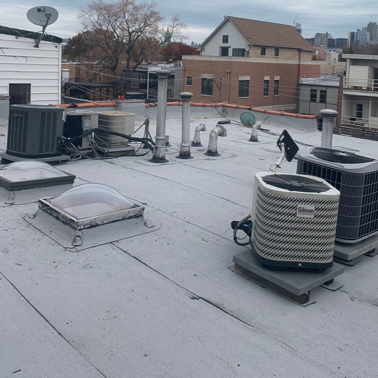 Snow-dusted rooftop with HVAC units, vents, and a city skyline in the background