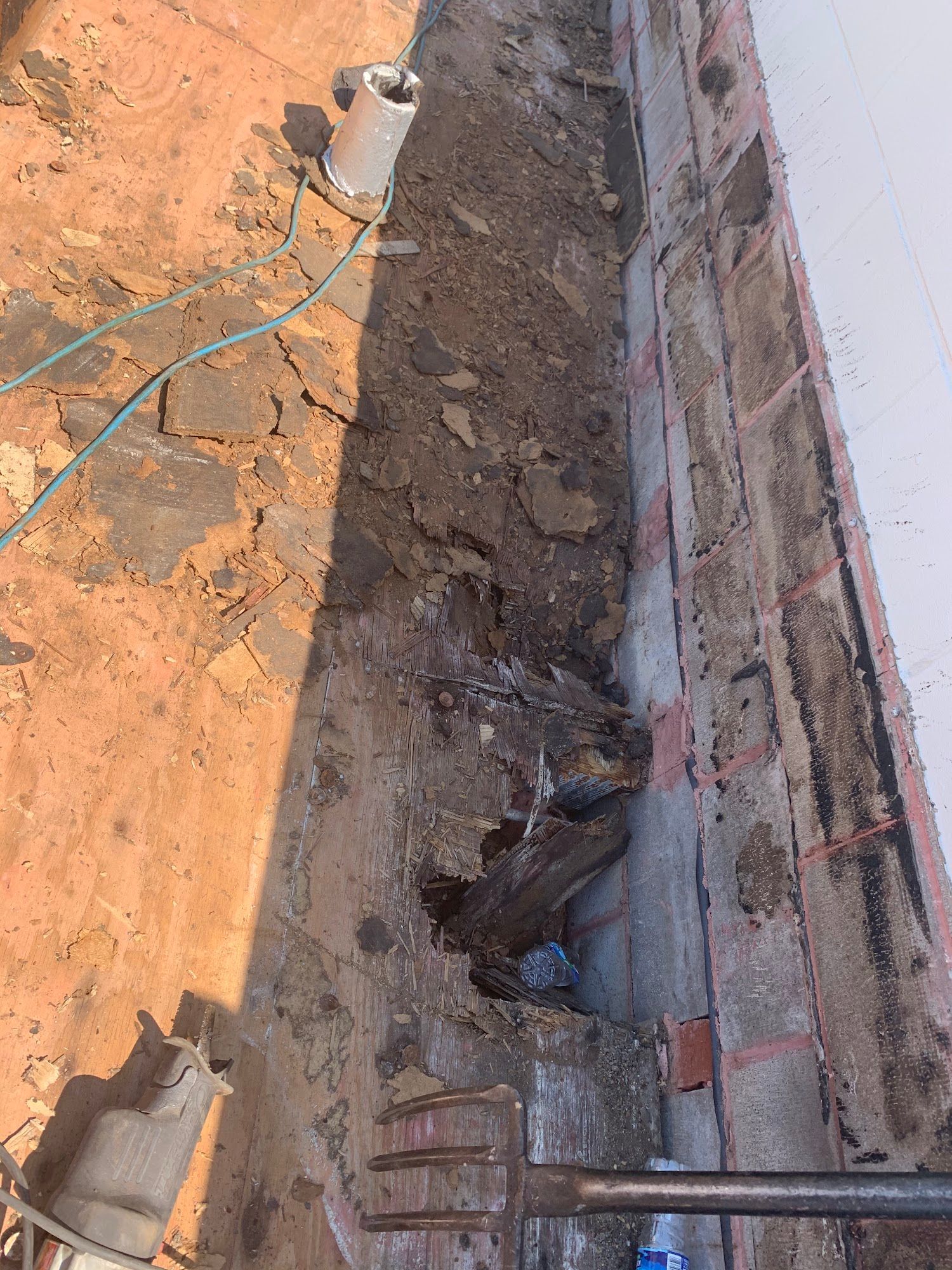 Trenched dirt strip beside a brick wall, with a shovel and wires on orange ground.