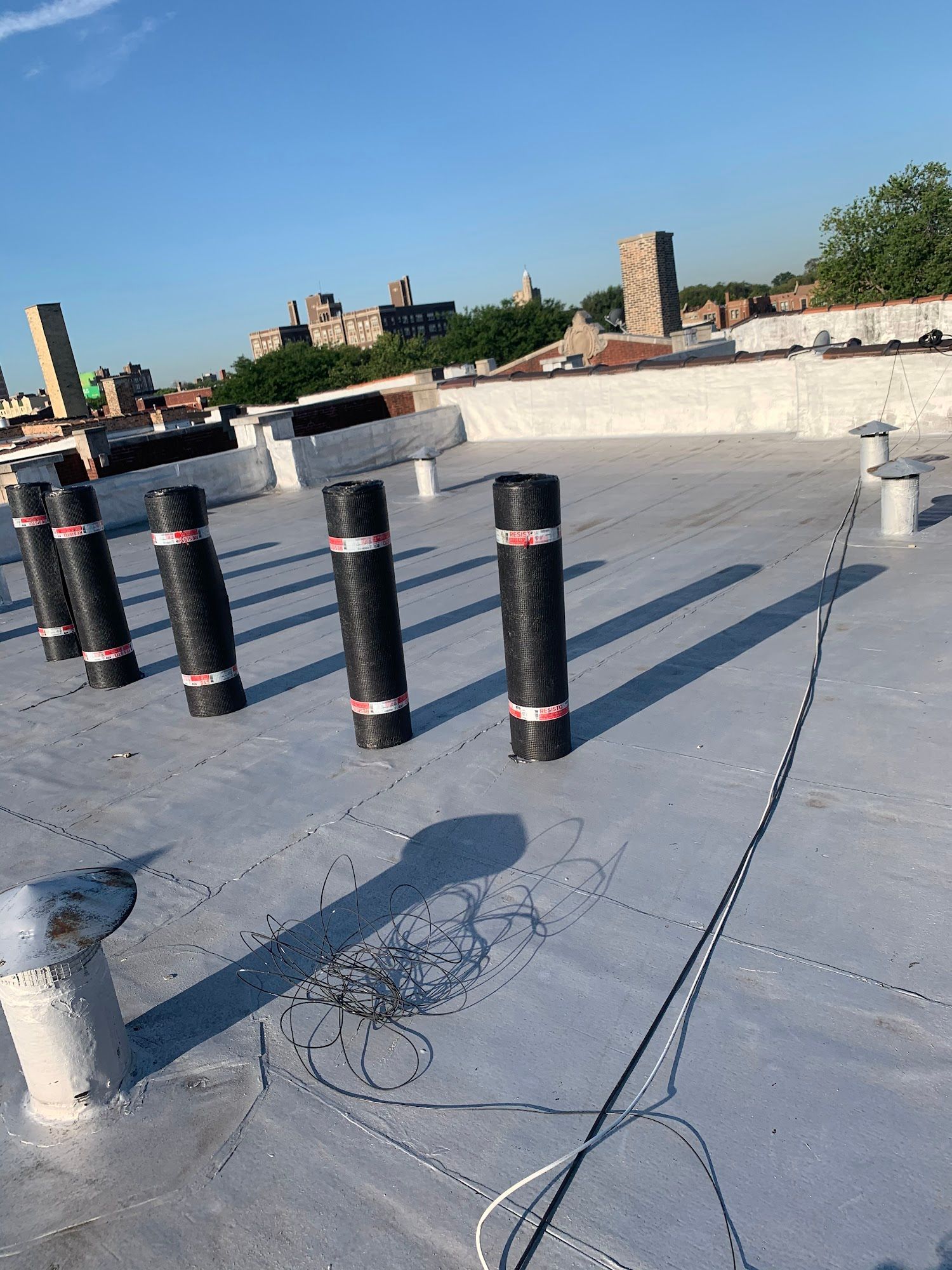 Flat rooftop with black vent pipes, cables, and a city skyline under a clear blue sky.