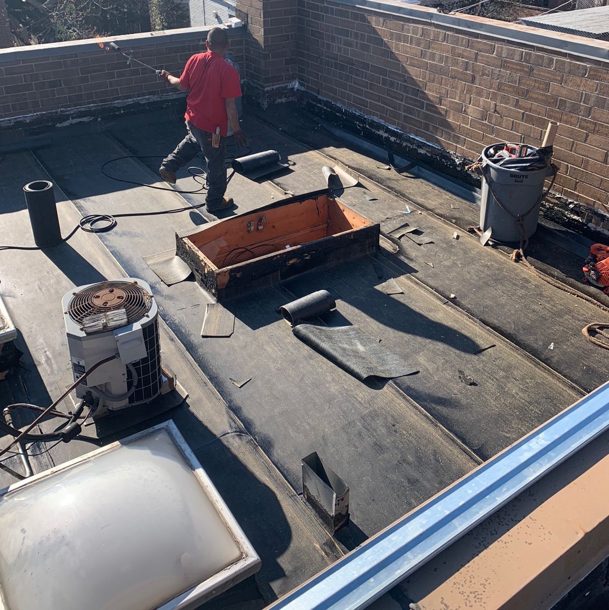 Roofer in red jacket on flat roof beside vents, skylight, and open roof hatch.