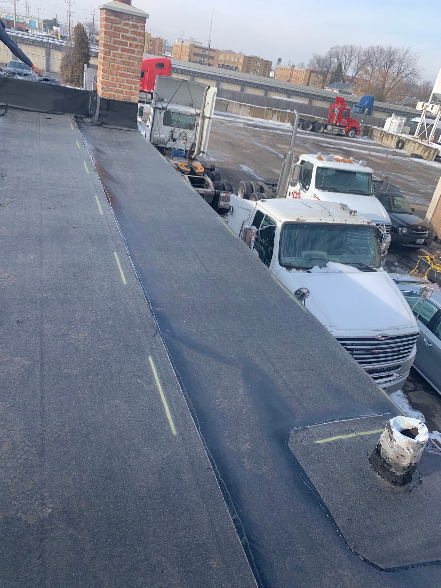 Snow-covered rooftop with a brick chimney and parked white trucks below under a winter sky