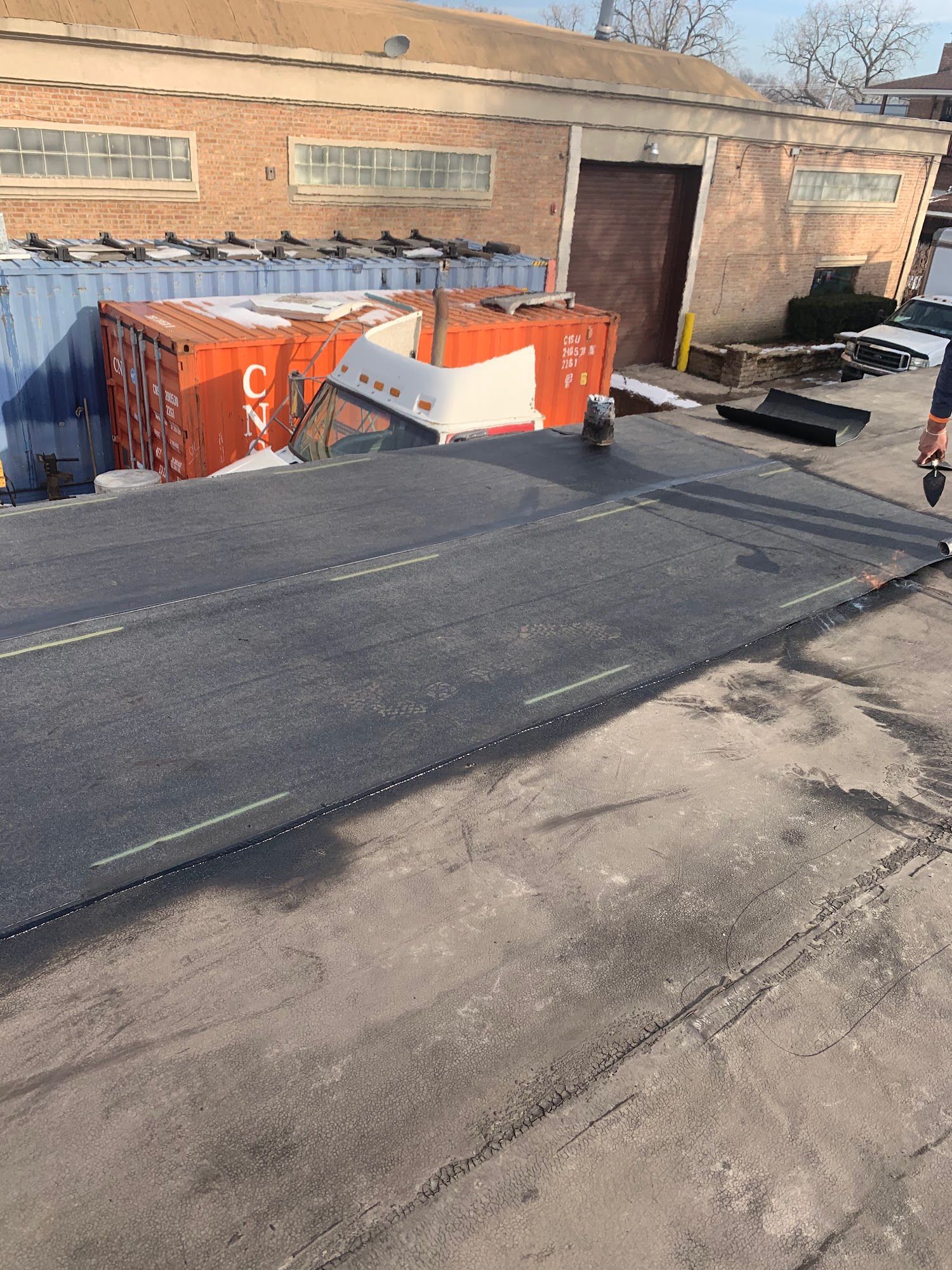 Black asphalt ramp beside an orange dumpster and brick building in an industrial yard
