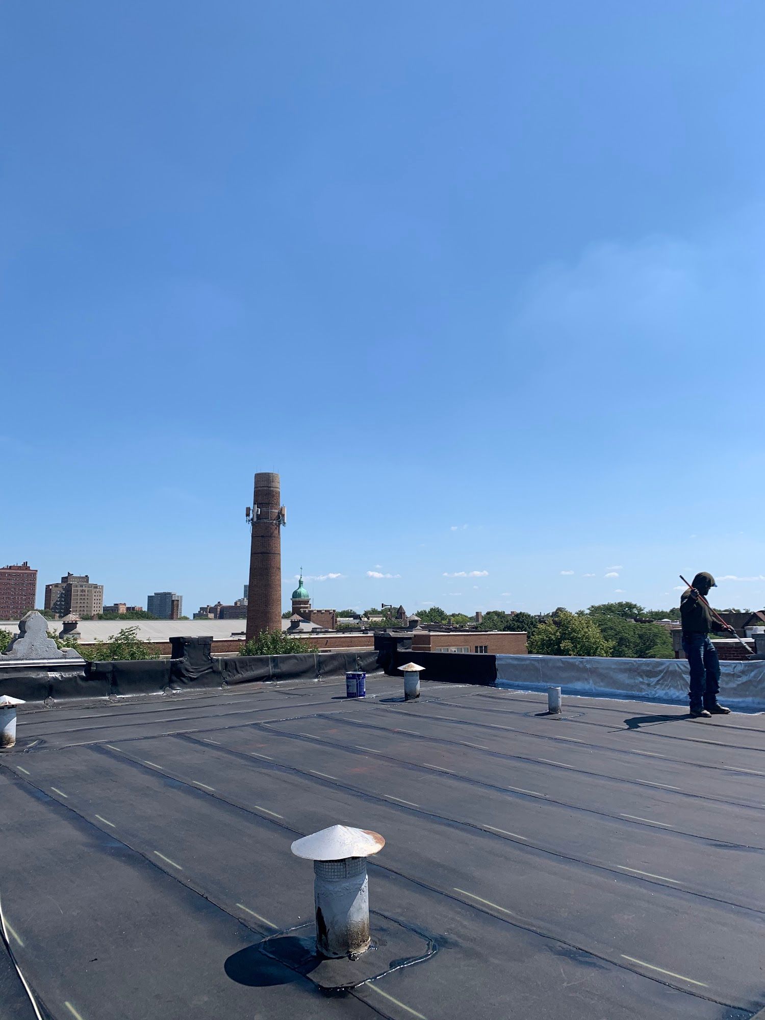 Rooftop with black surface, vents, blue sky, and one person standing near the edge.