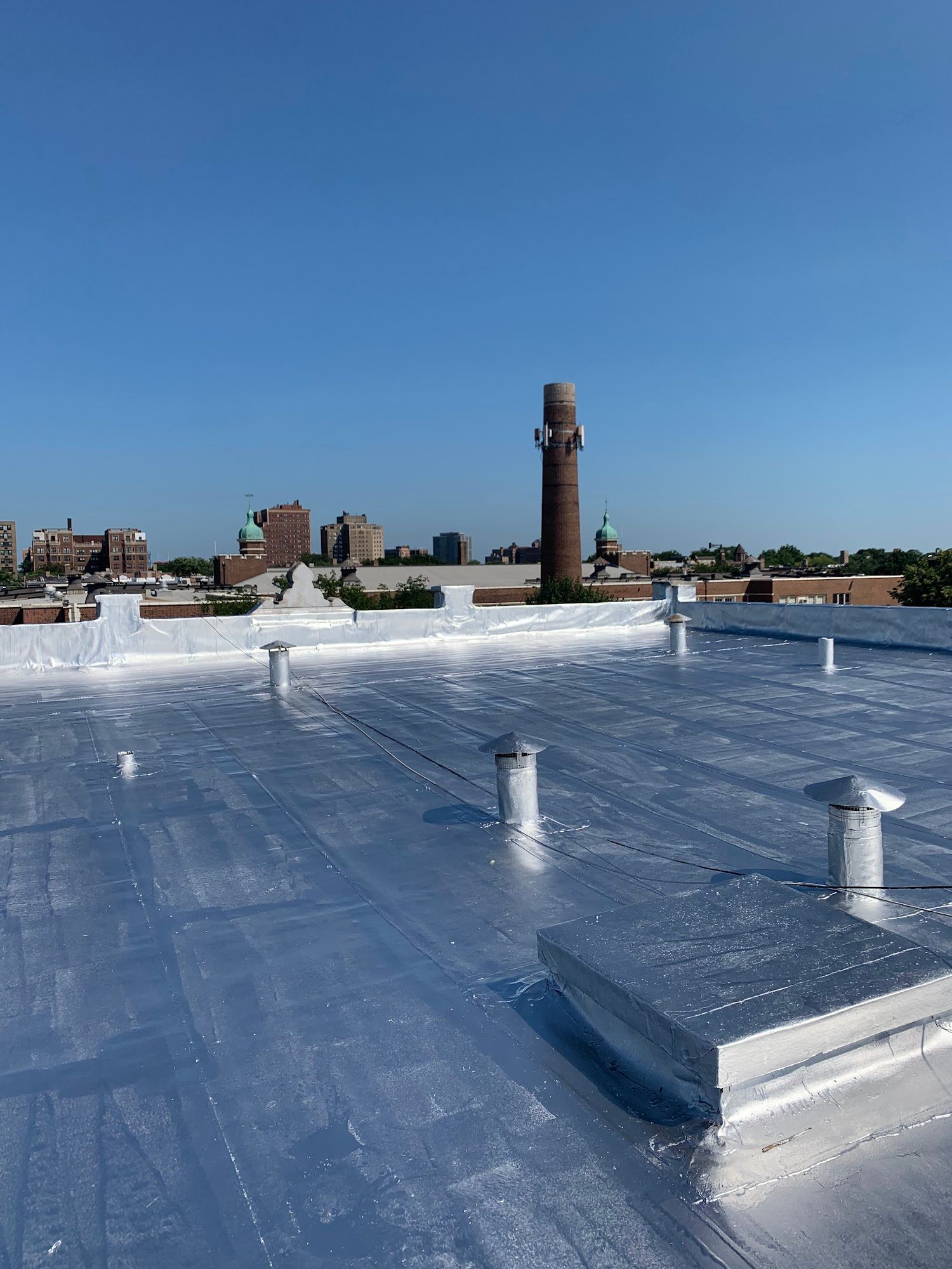 Rooftop with white gravel, skylights, and a brick chimney under a clear blue sky.