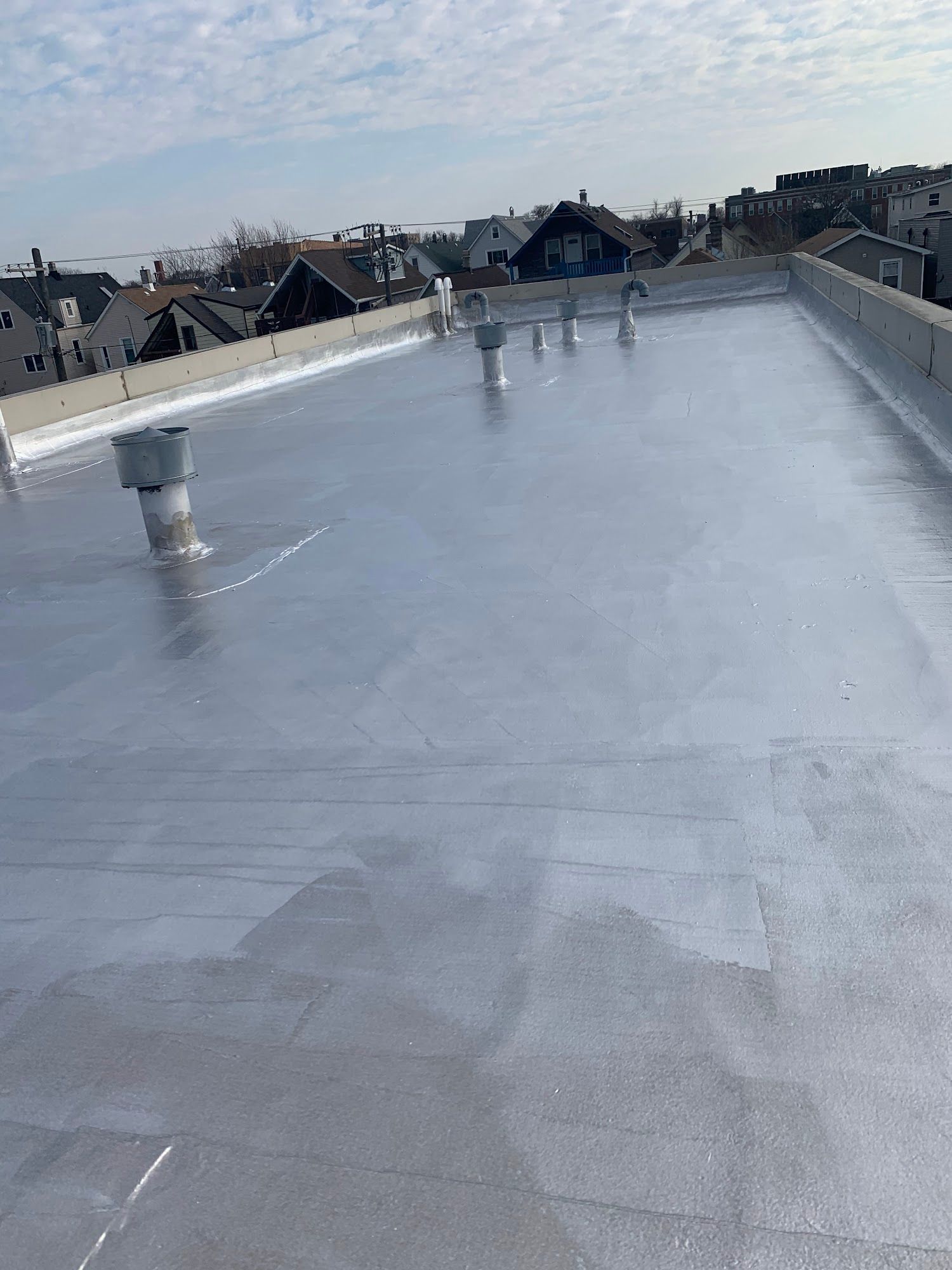 Flat gray rooftop with vents, reflecting water, and distant houses under a cloudy sky.