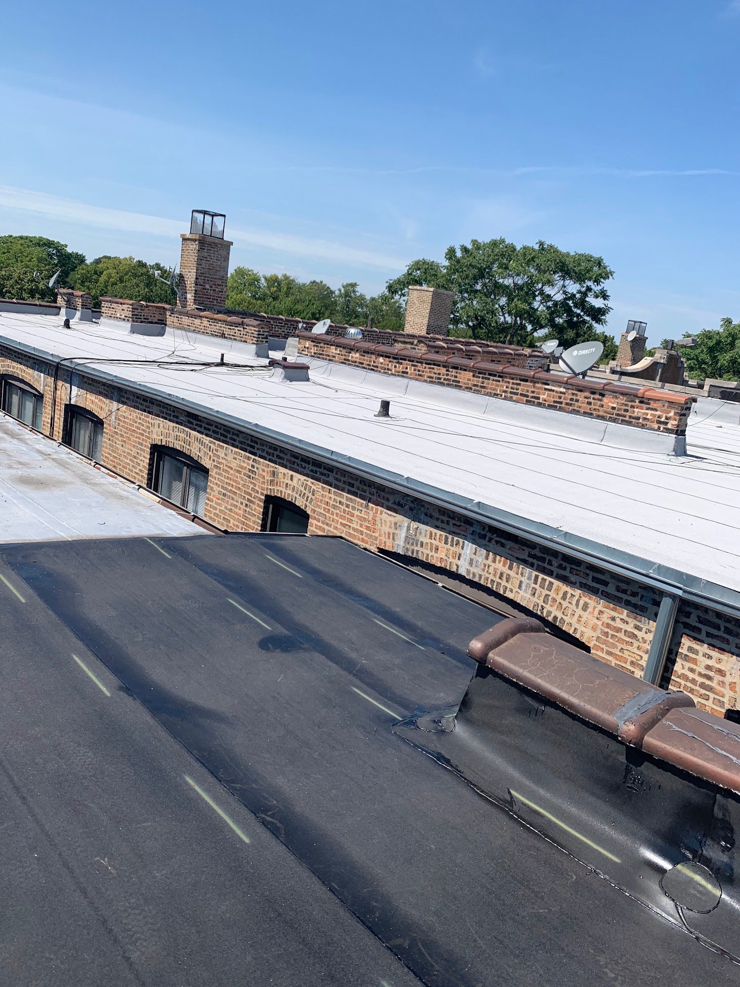 Rooftops with a white metal roof, black flat roof, and brick chimney stacks under a blue sky