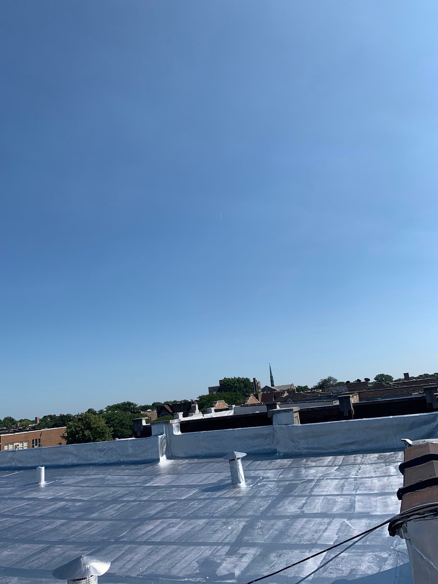 Blue sky over a silver metal rooftop with vents and distant trees and buildings