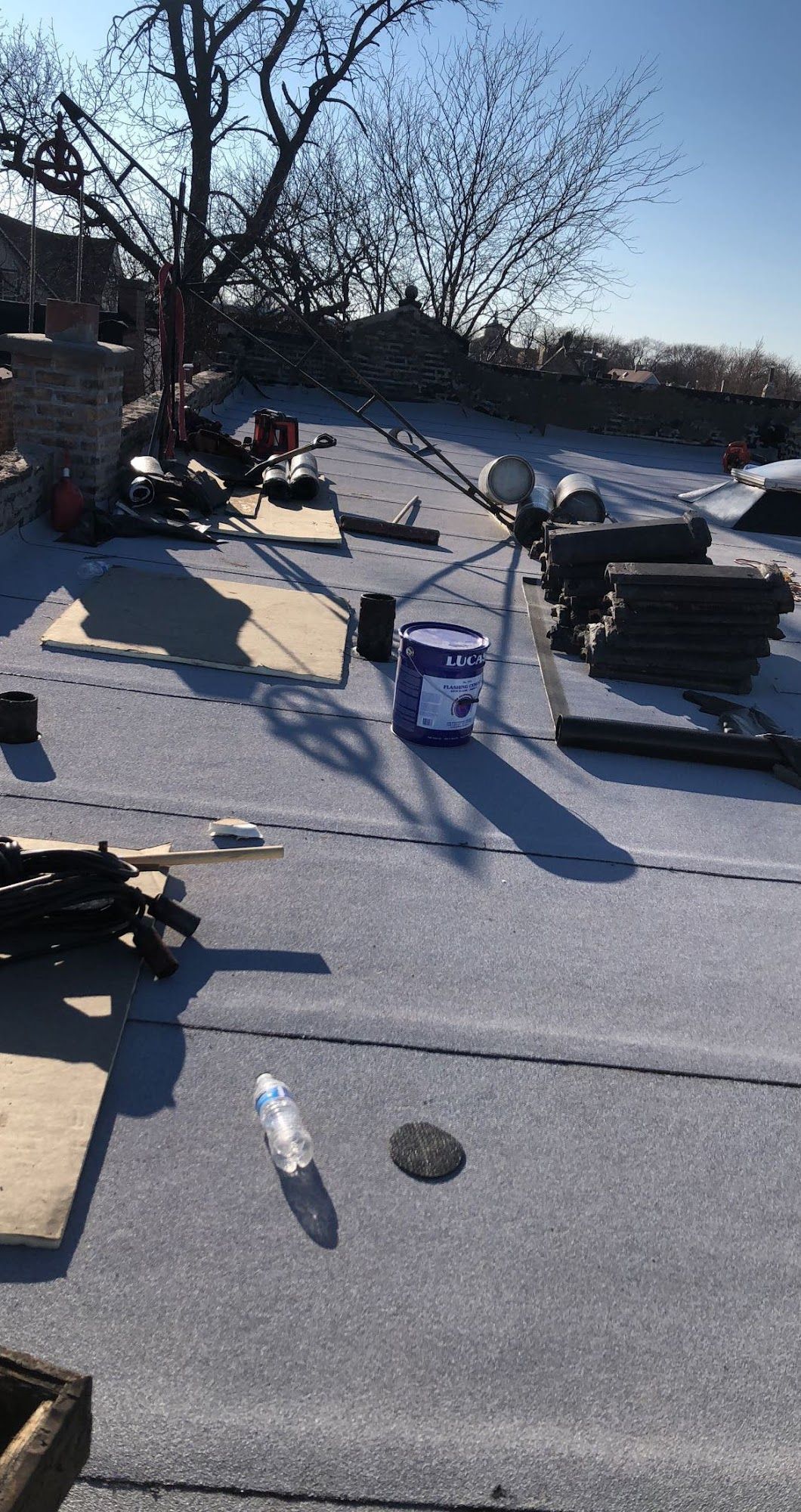 Snow-covered rooftop with scattered tools, buckets, and construction materials under a blue sky