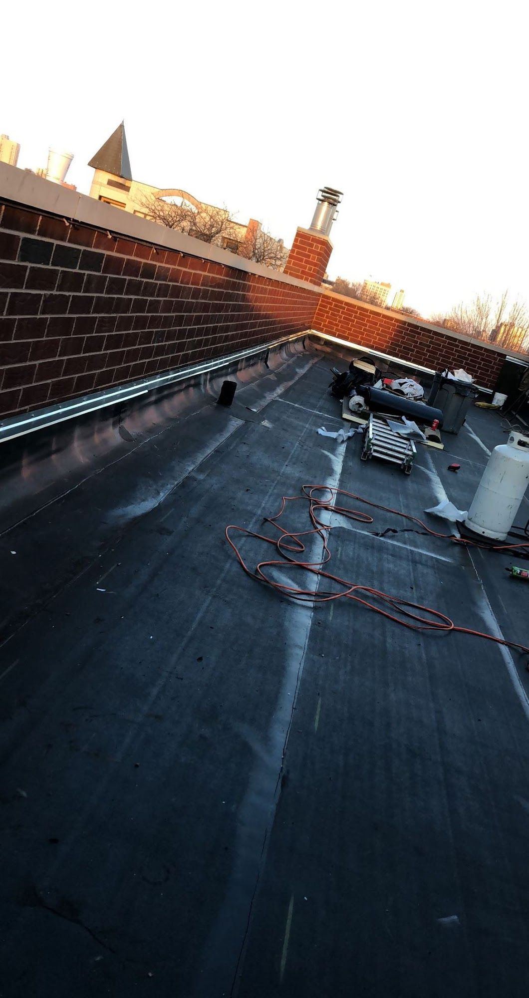 Rooftop at sunset with a brick parapet, vents, and cables on a dark tar surface
