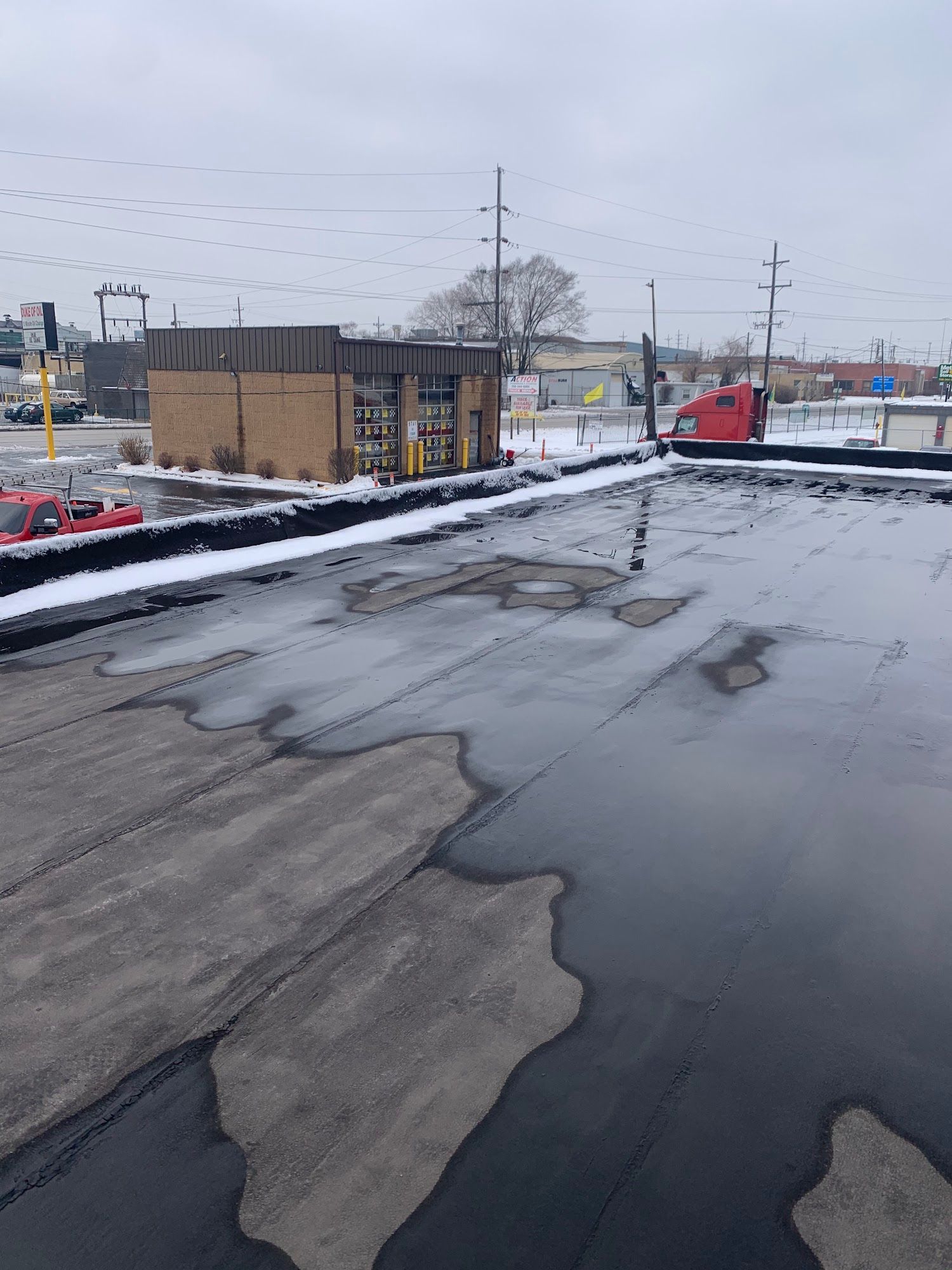 Snowy industrial rooftop with puddles, cracked pavement, and utility poles under an overcast sky