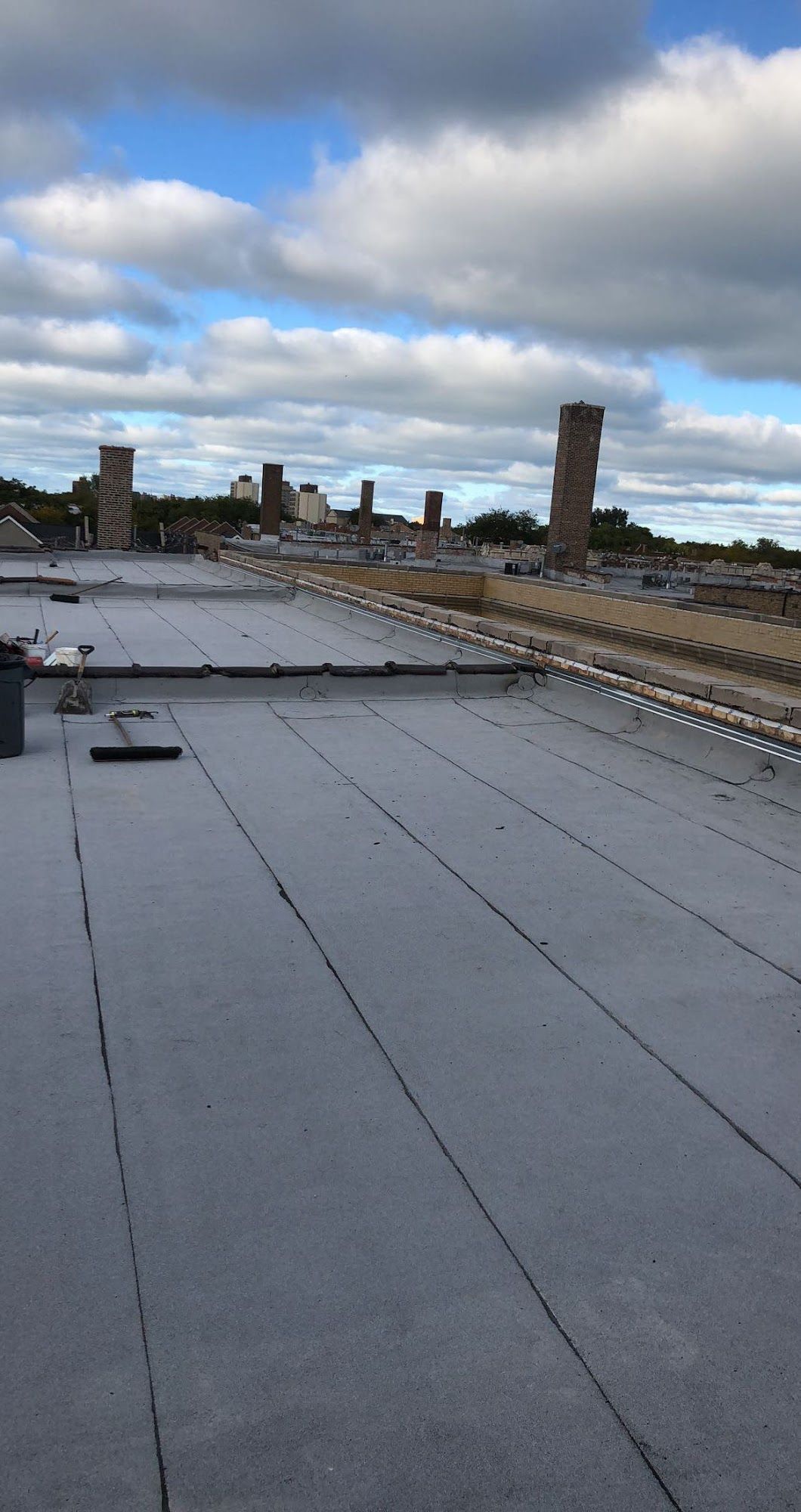 Rooftop with flat gray membrane and city skyline under cloudy blue sky