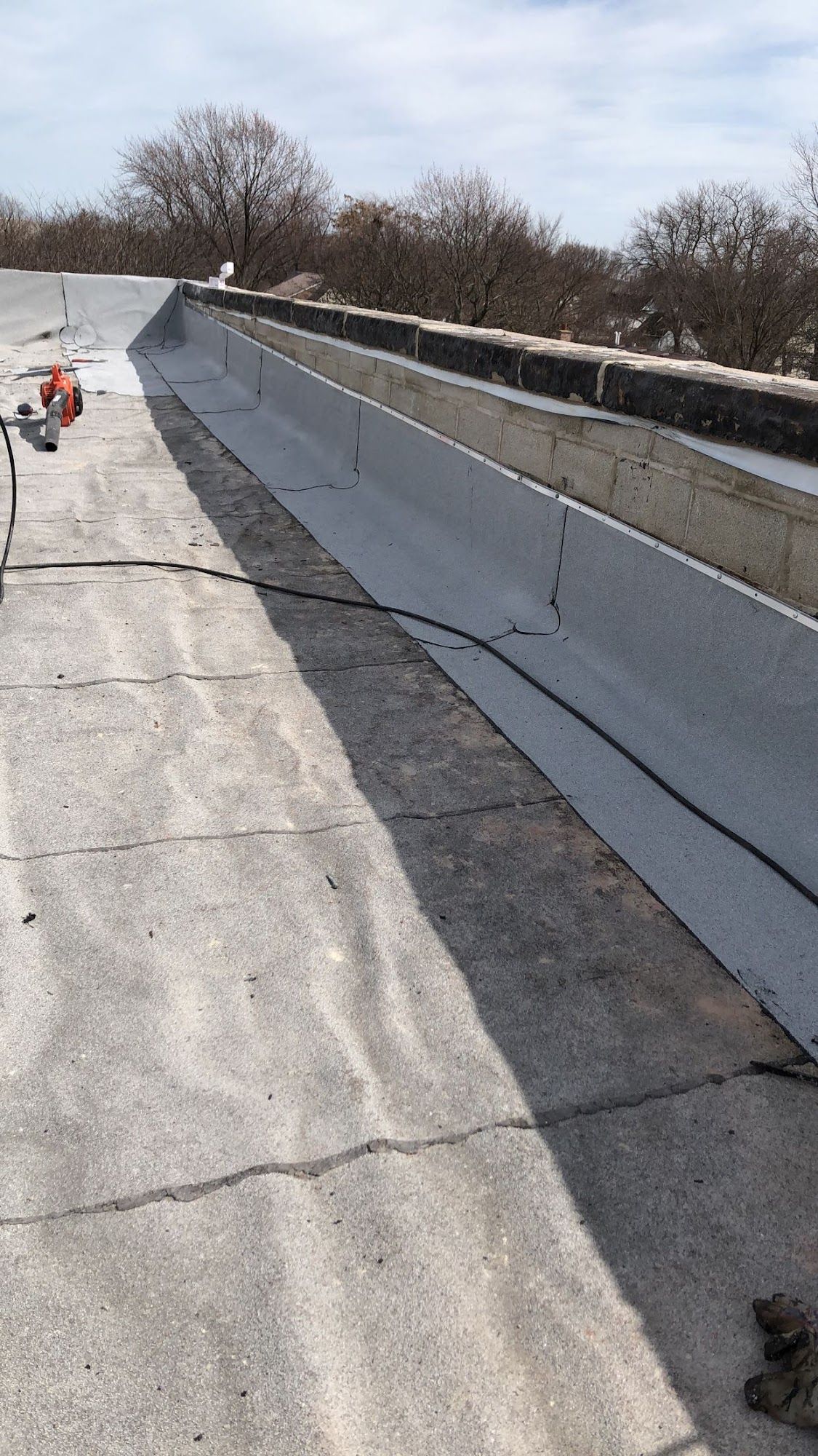 Damaged concrete rooftop with long cracks and a raised parapet wall under a cloudy sky