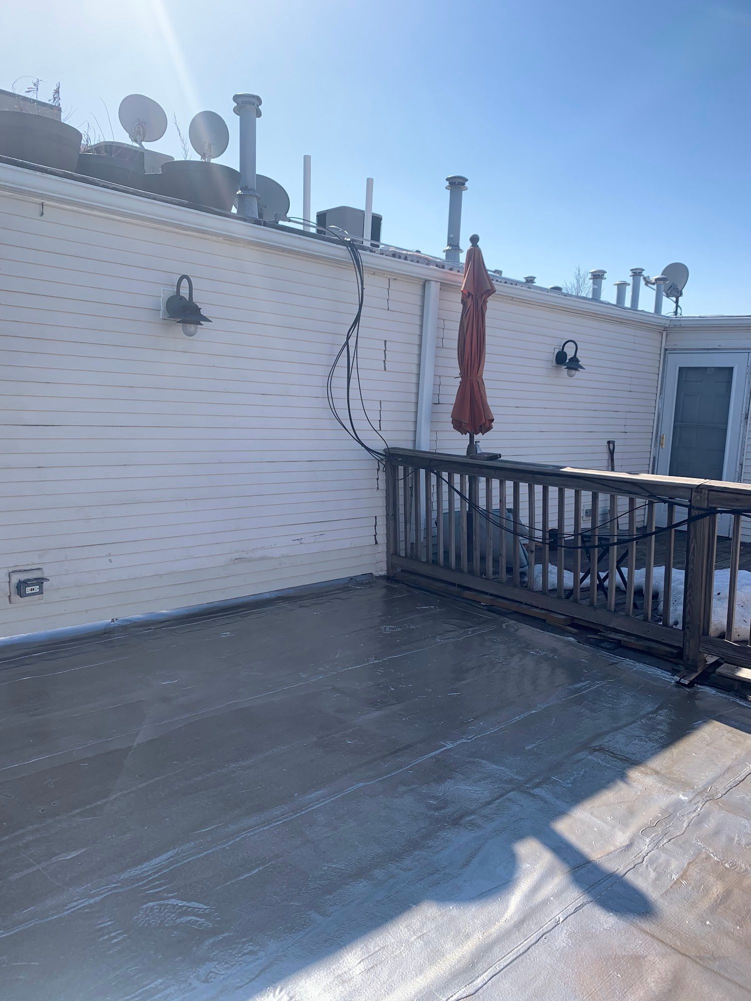 Rooftop patio with white brick wall, railings, antennas, and a closed red umbrella in bright sunlight