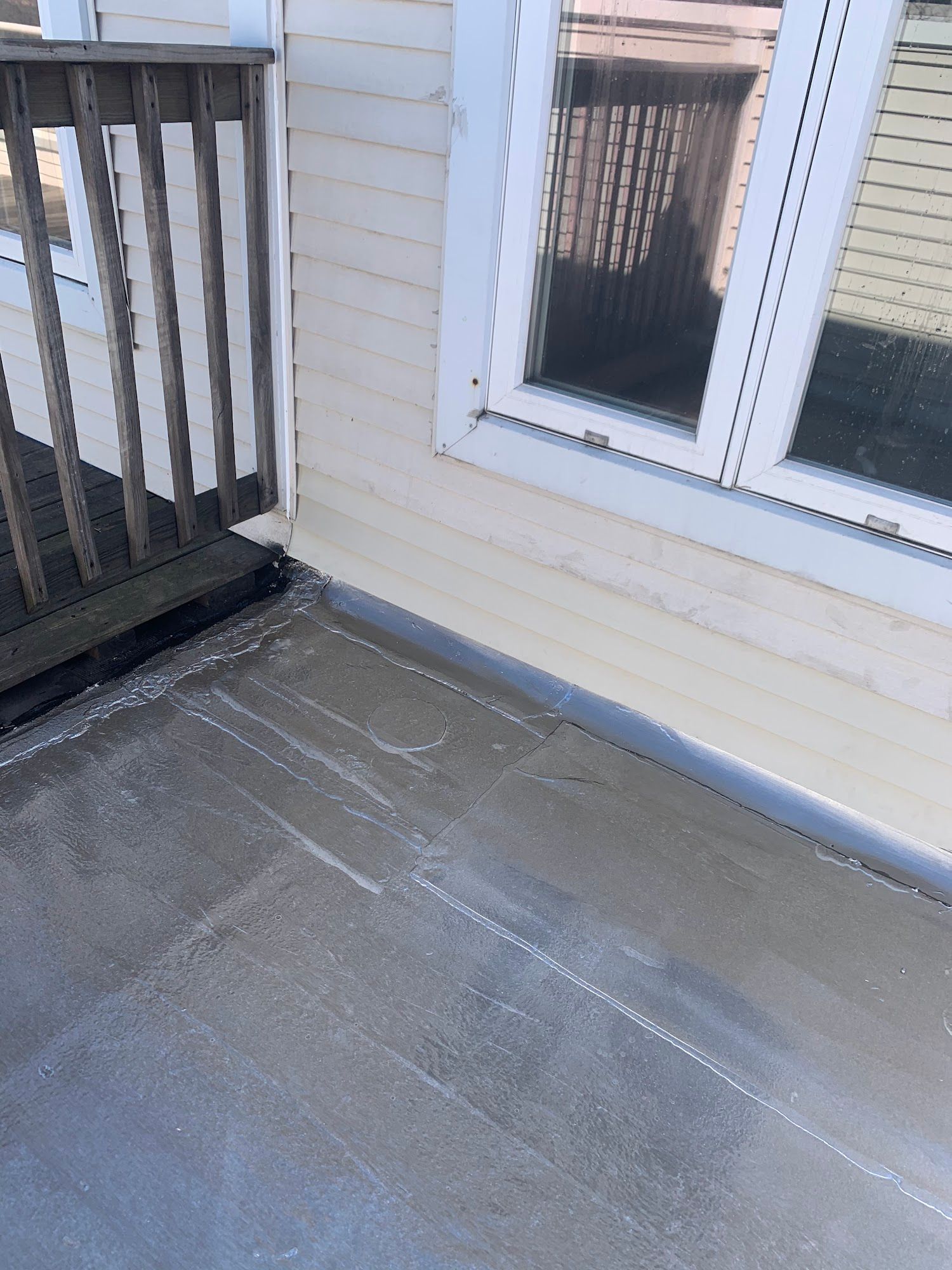 Concrete balcony corner beside beige siding and a window, with white railing on the left.