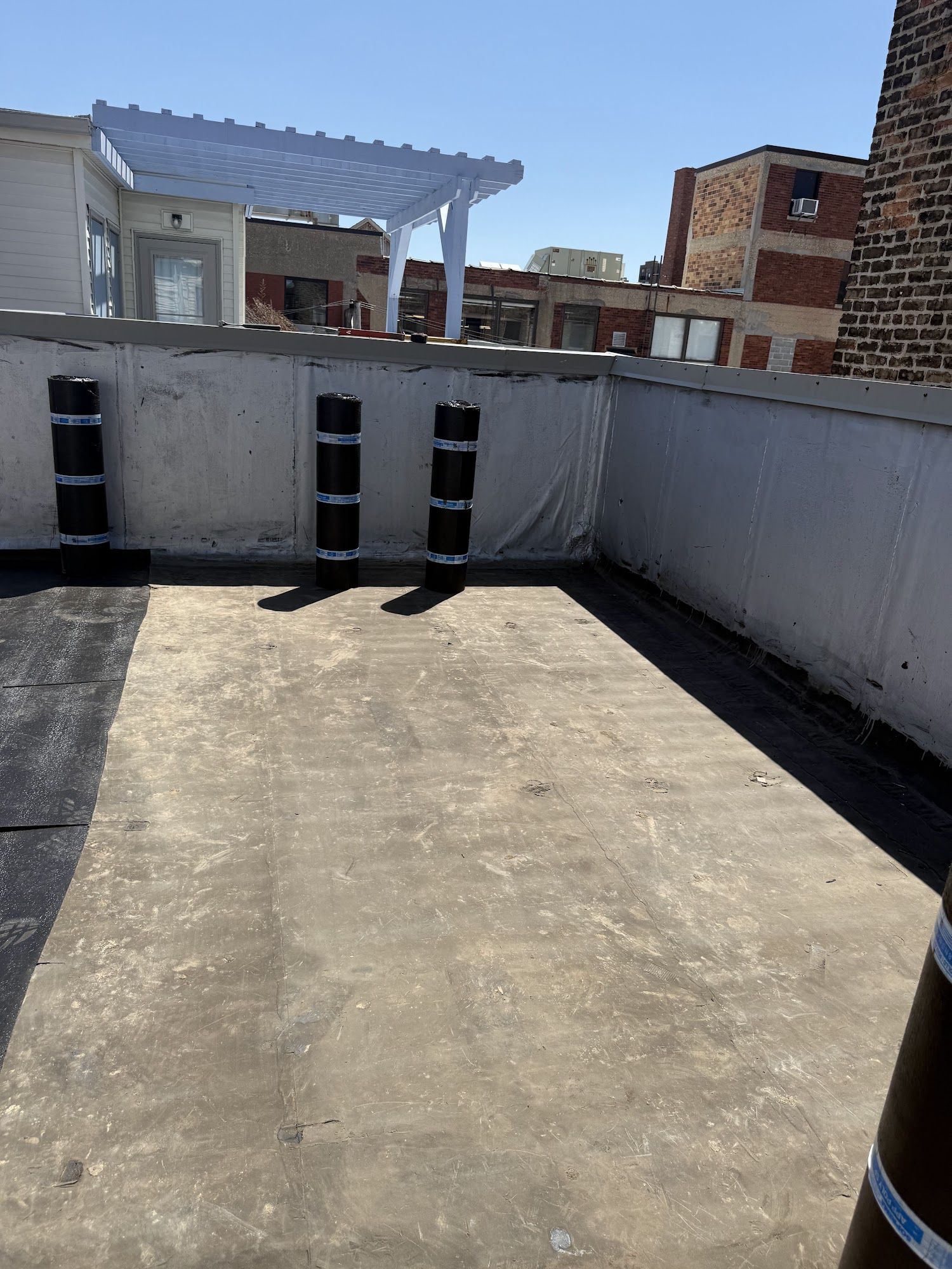 Rooftop patio with white fence, concrete floor, and striped black-and-white posts under bright sunlight