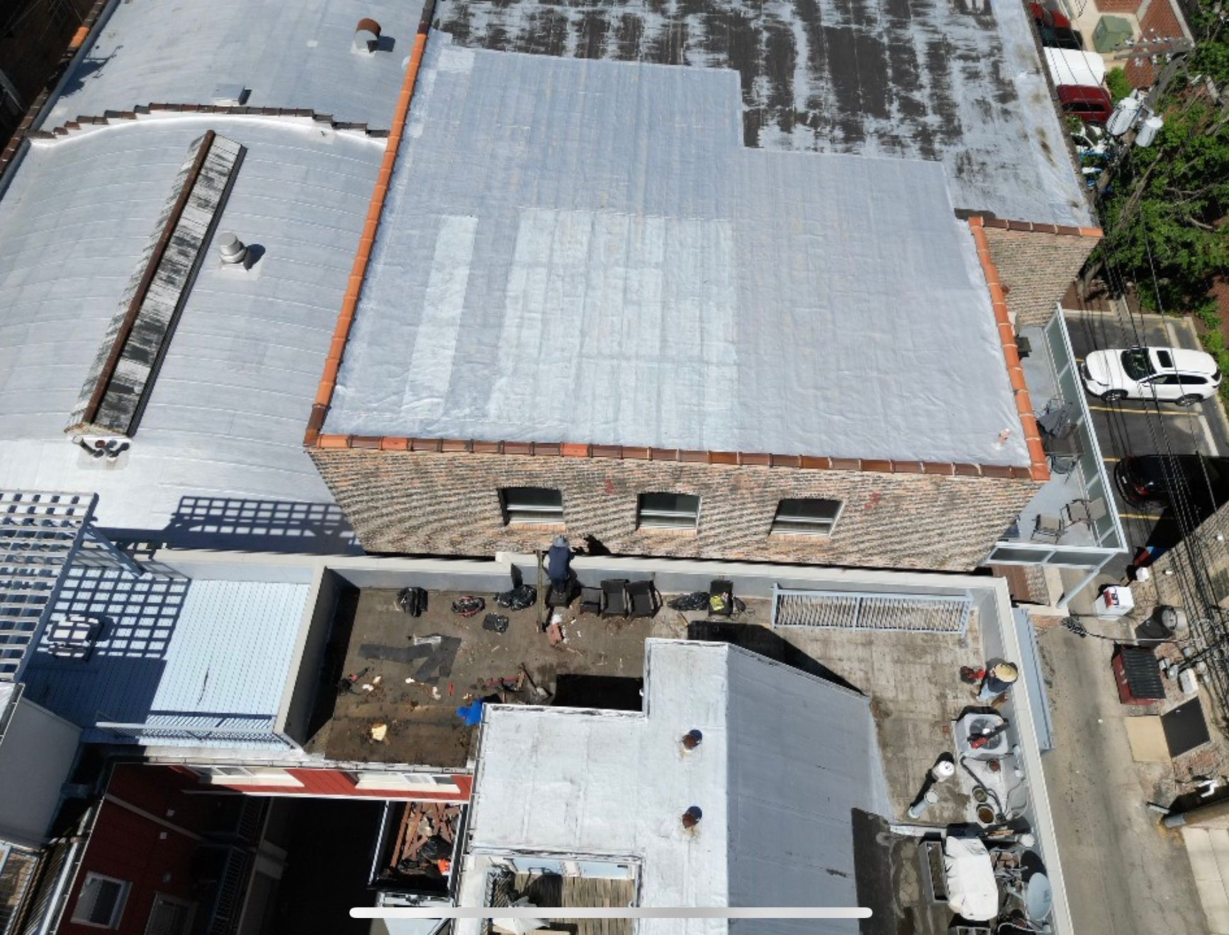Aerial view of an industrial building with a large gray roof and adjacent yard with vehicles and equipment