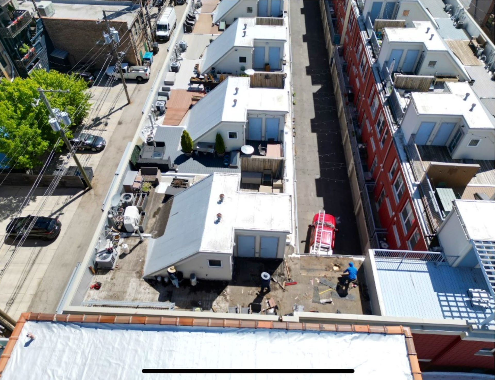 Aerial view of a row of white trailers and buildings along a narrow street, with parked cars and construction scaffolding.