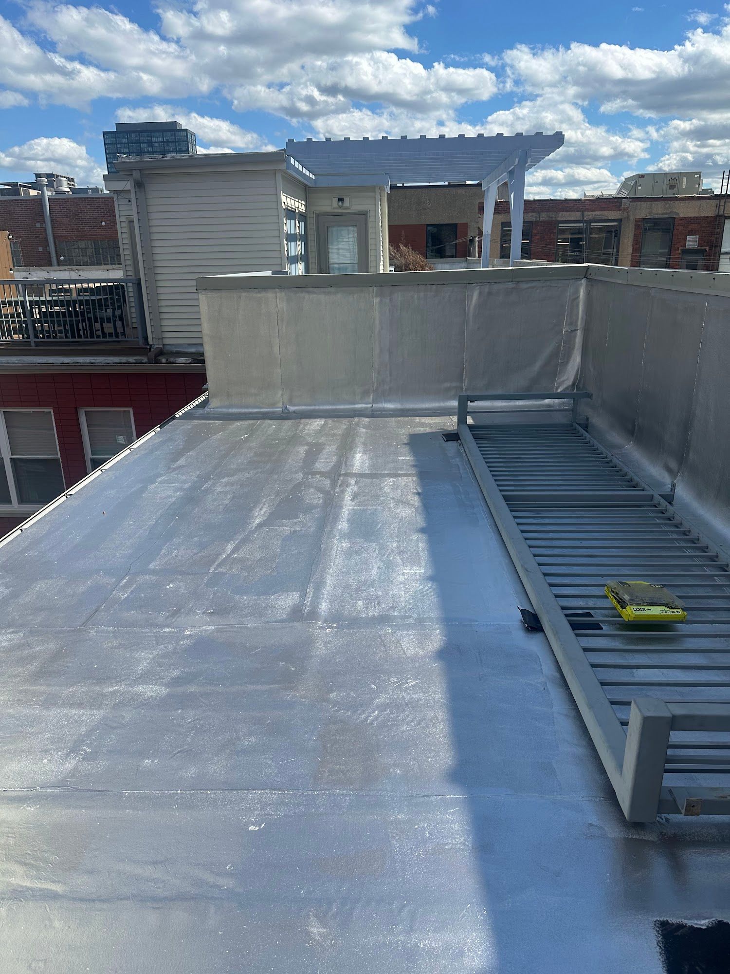 Rooftop with silver waterproof membrane, skylight, and ladder against a cloudy sky.